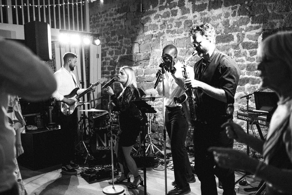 Full wedding band performing live at Tithe Barn Symondsbury Dorset with singer, guitarist and saxophonist during barn reception entertainment
