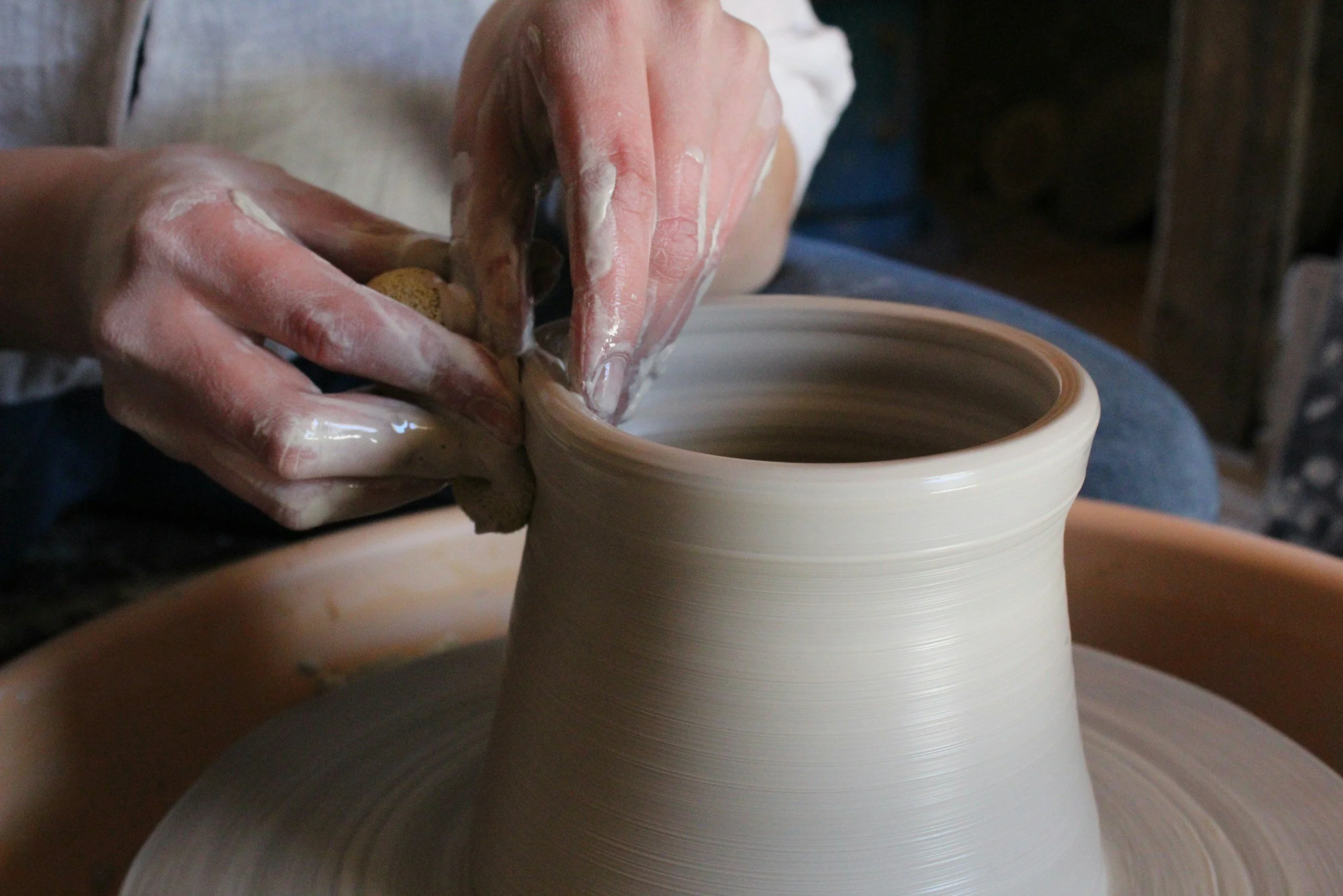 A person shaping a clay vase on a pottery wheel, using their hands coated in wet clay.