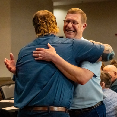 Two men hugging and smiling at each other in a social setting.