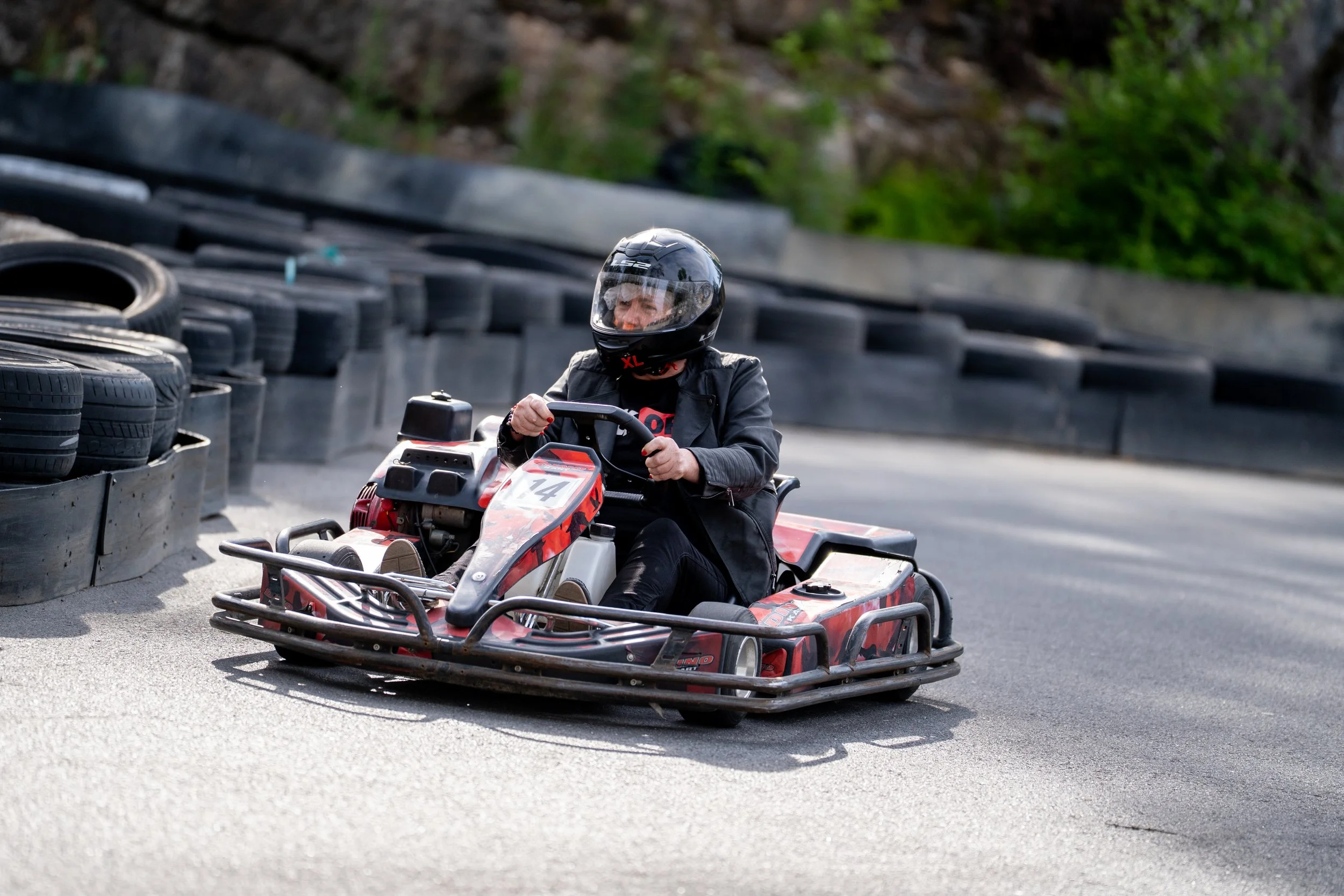 Person in a safety helmet driving a go-kart on a race track with tire barriers along the side.