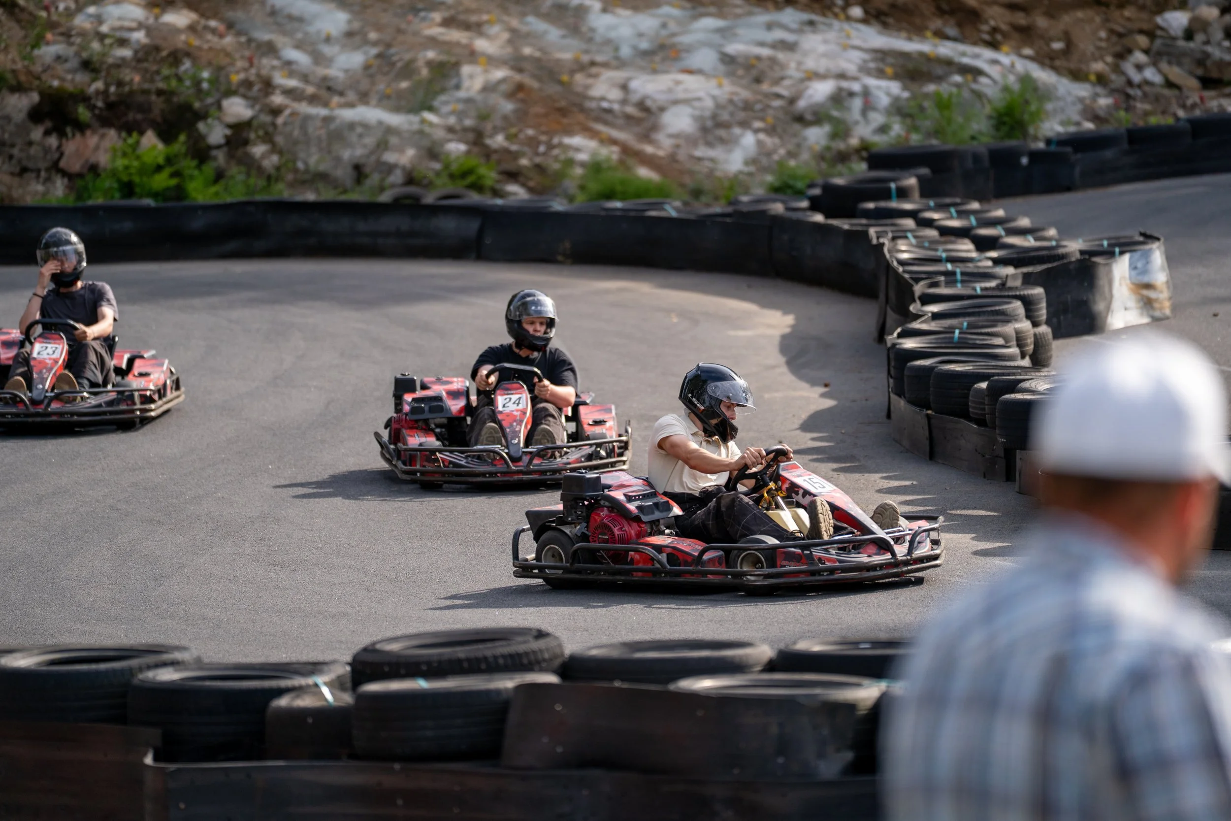 People racing go-karts on an outdoor track marked by black tires used as barriers.