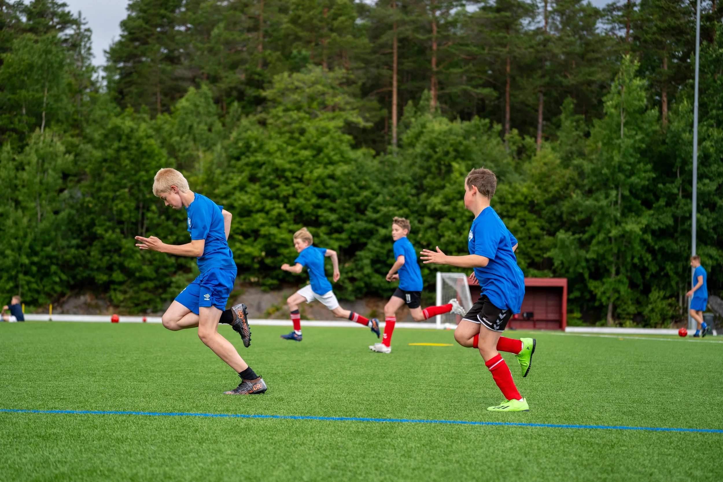 Young boys in blue jerseys running on a soccer field during training or practice.