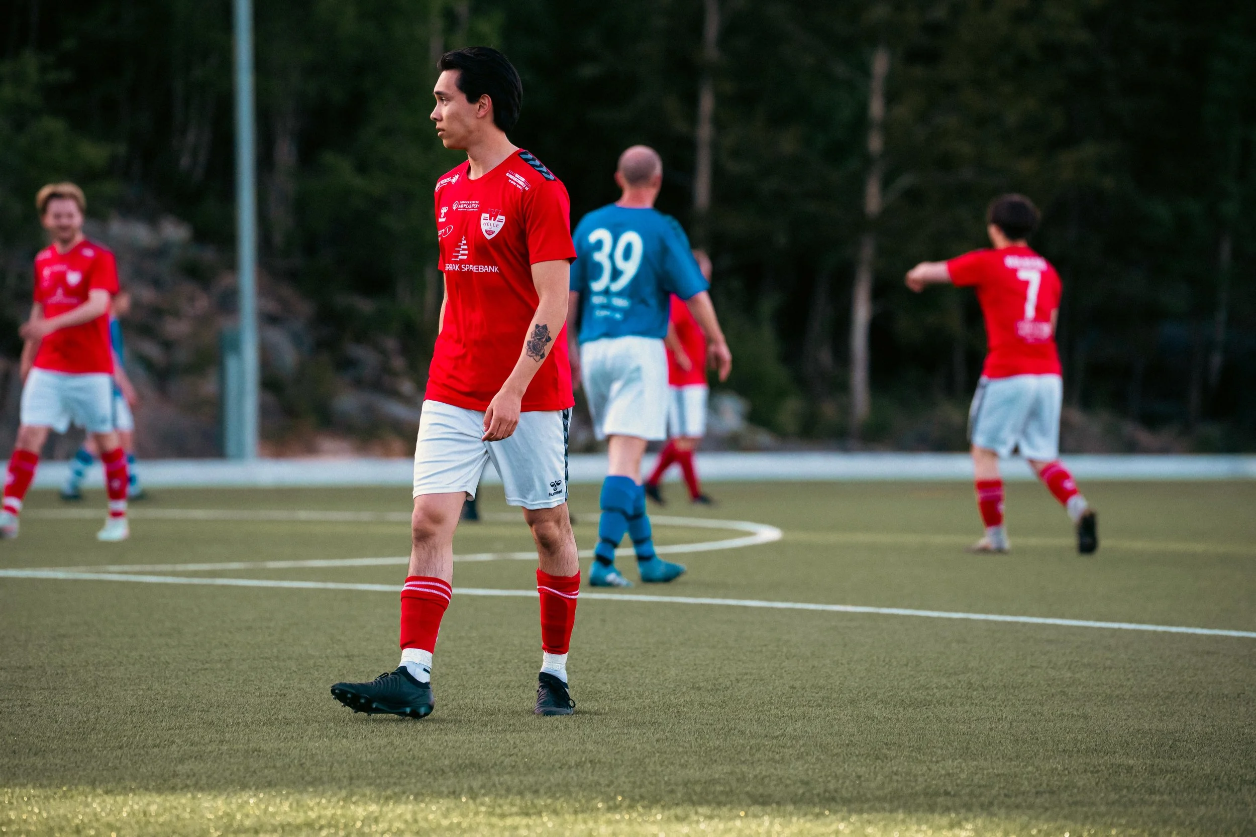 Soccer players on the field during a game, with one player in focus looking down and others in the background with arms outstretched.