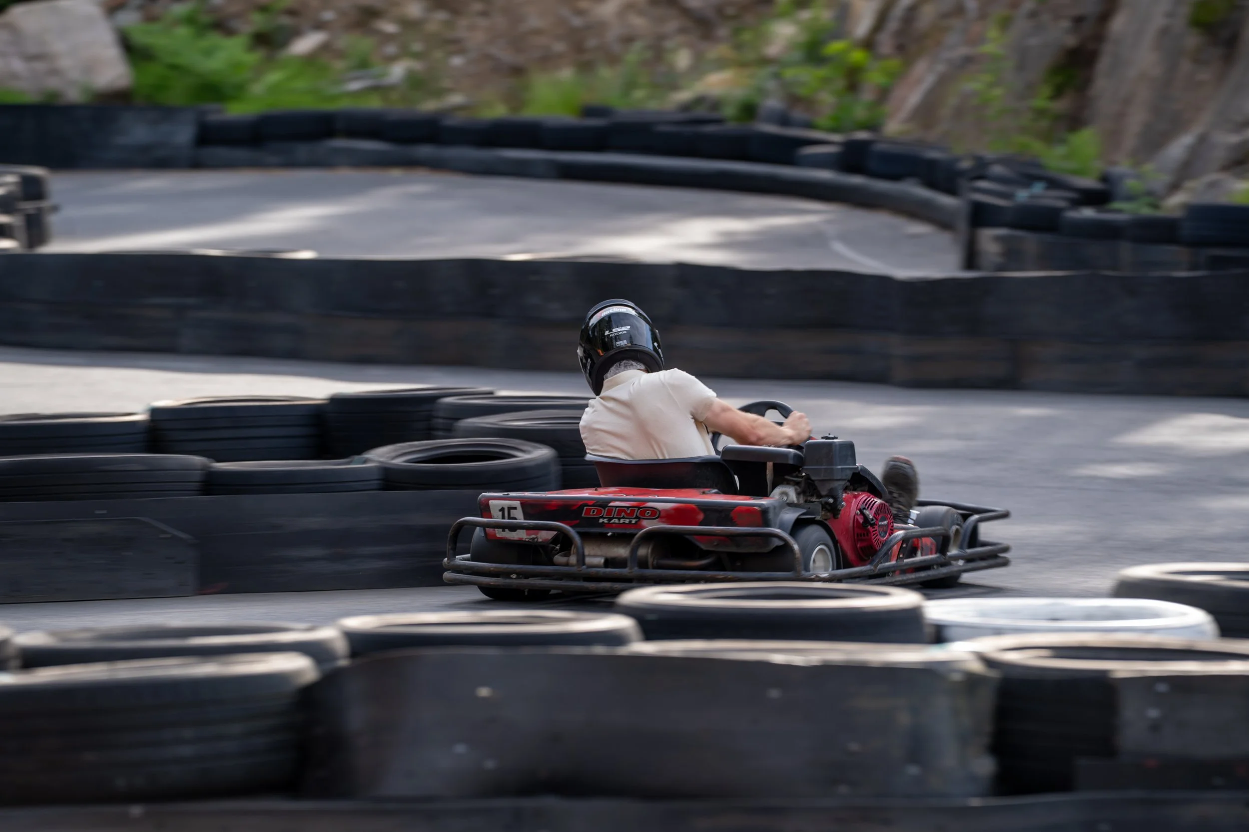 Person driving a go-kart on an outdoor race track with tire barriers.