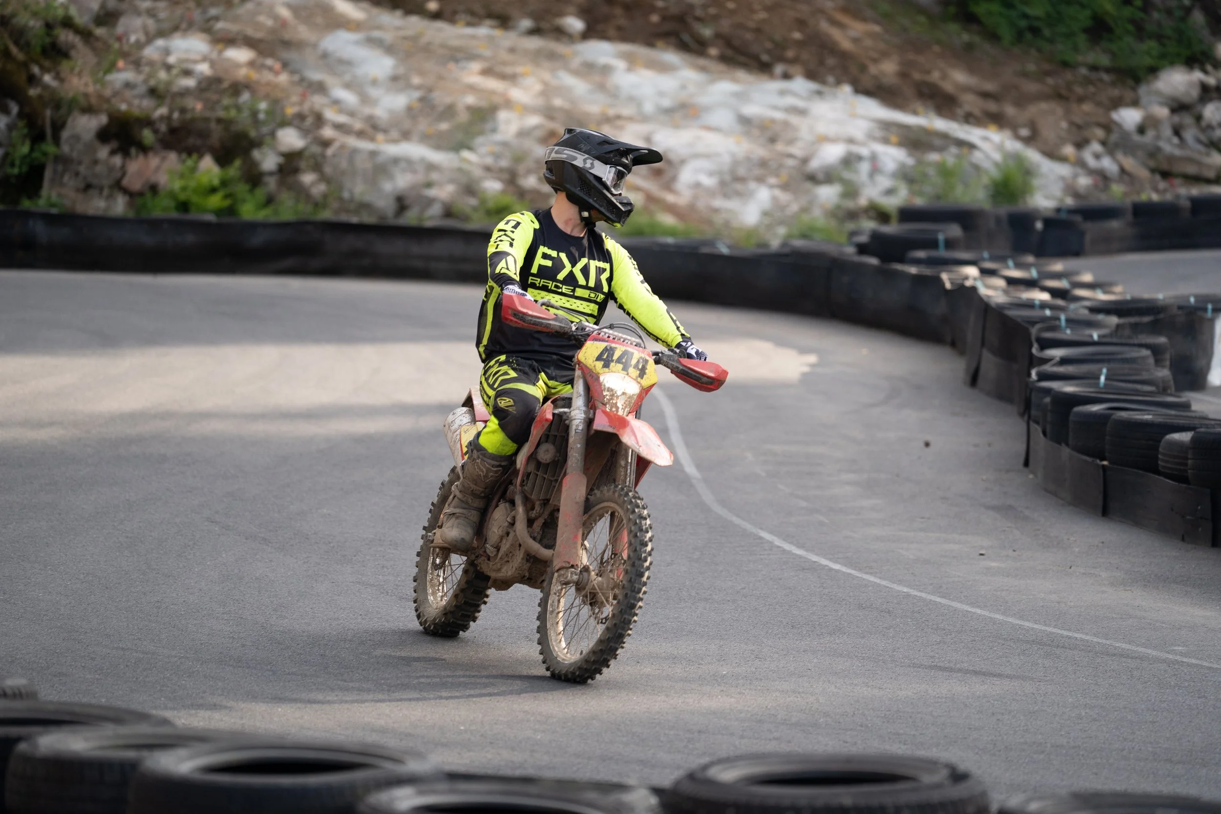 A person riding a dirt bike on a paved track surrounded by black tires used as barriers during a motocross race.