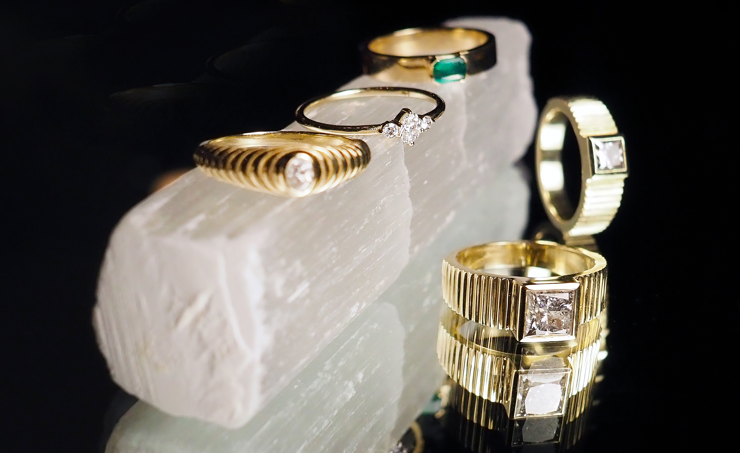A collection of gold and silver rings with diamonds displayed on a light-colored stone, against a dark background.