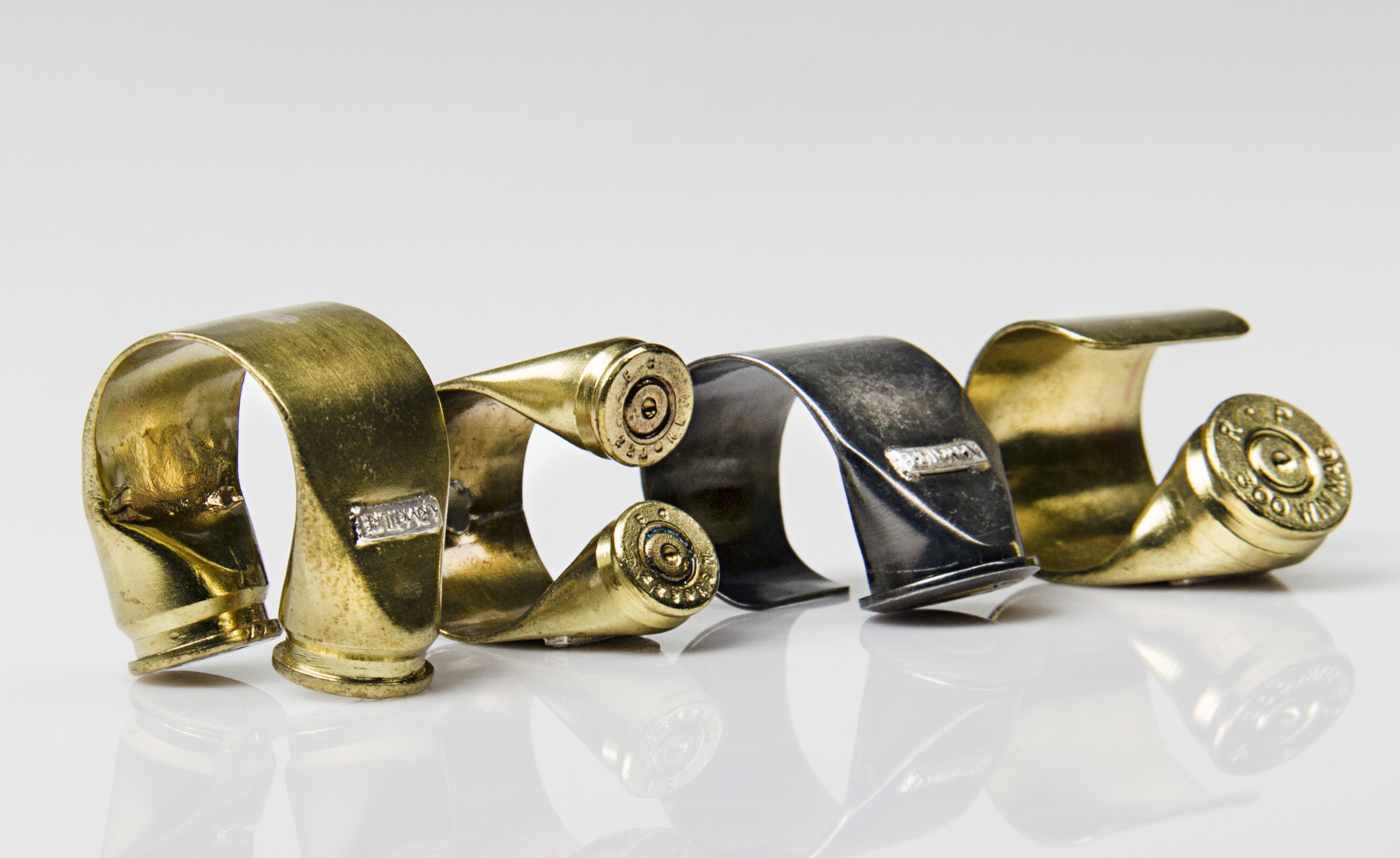 Twisted and bent brass and metal shotgun shells on a reflective white surface.