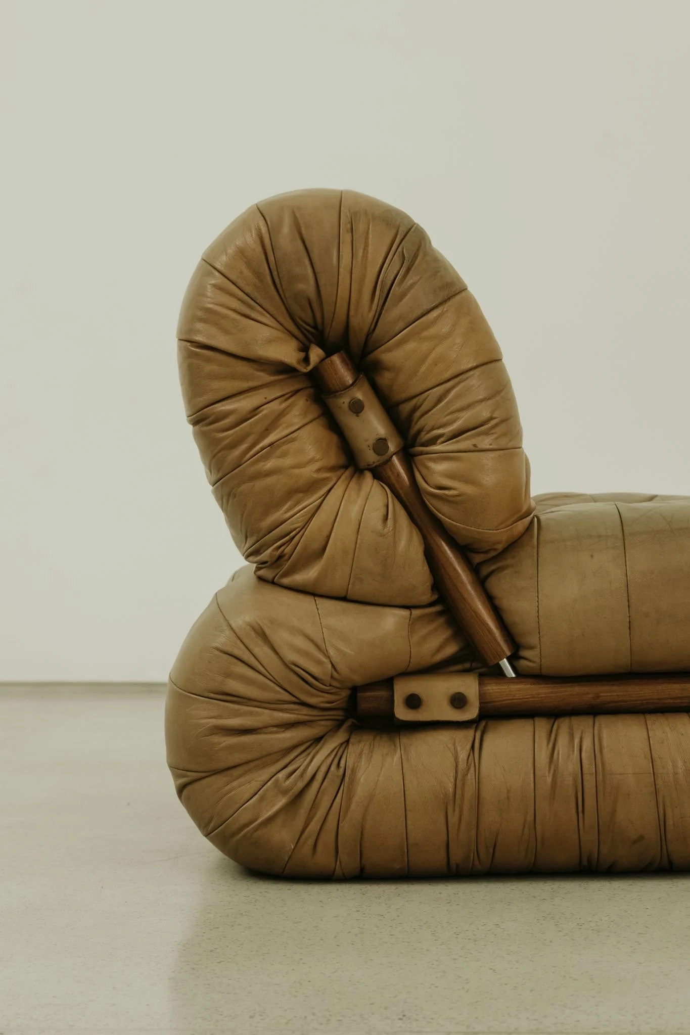 Close-up of a vintage-style beige leather armchair with wooden armrests, set against a plain white background.