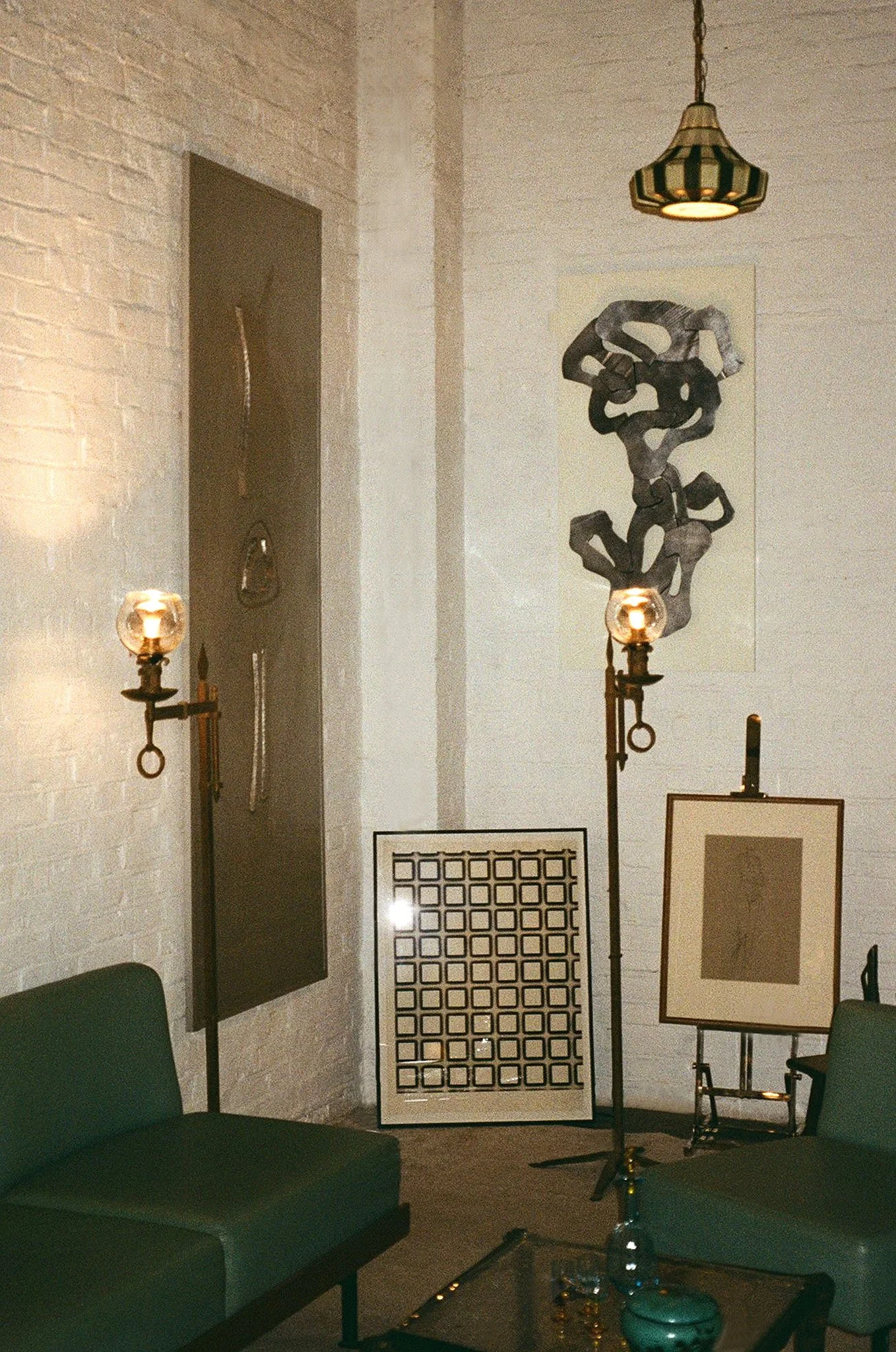 Interior room with modern artwork, a lamp, and furniture including green chairs and a glass coffee table.