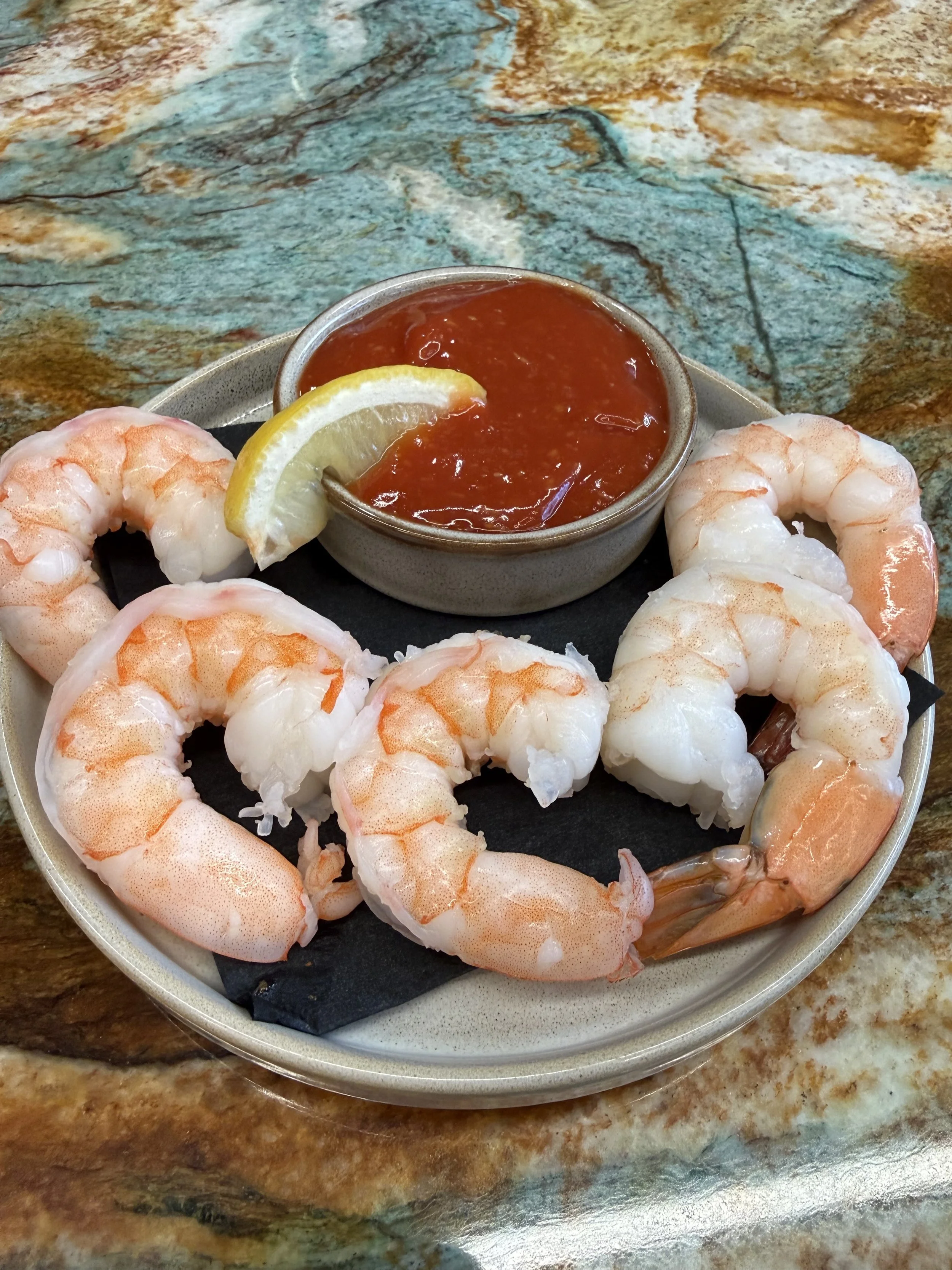 Shrimp with a lemon wedge and cocktail sauce in a bowl on a plate.