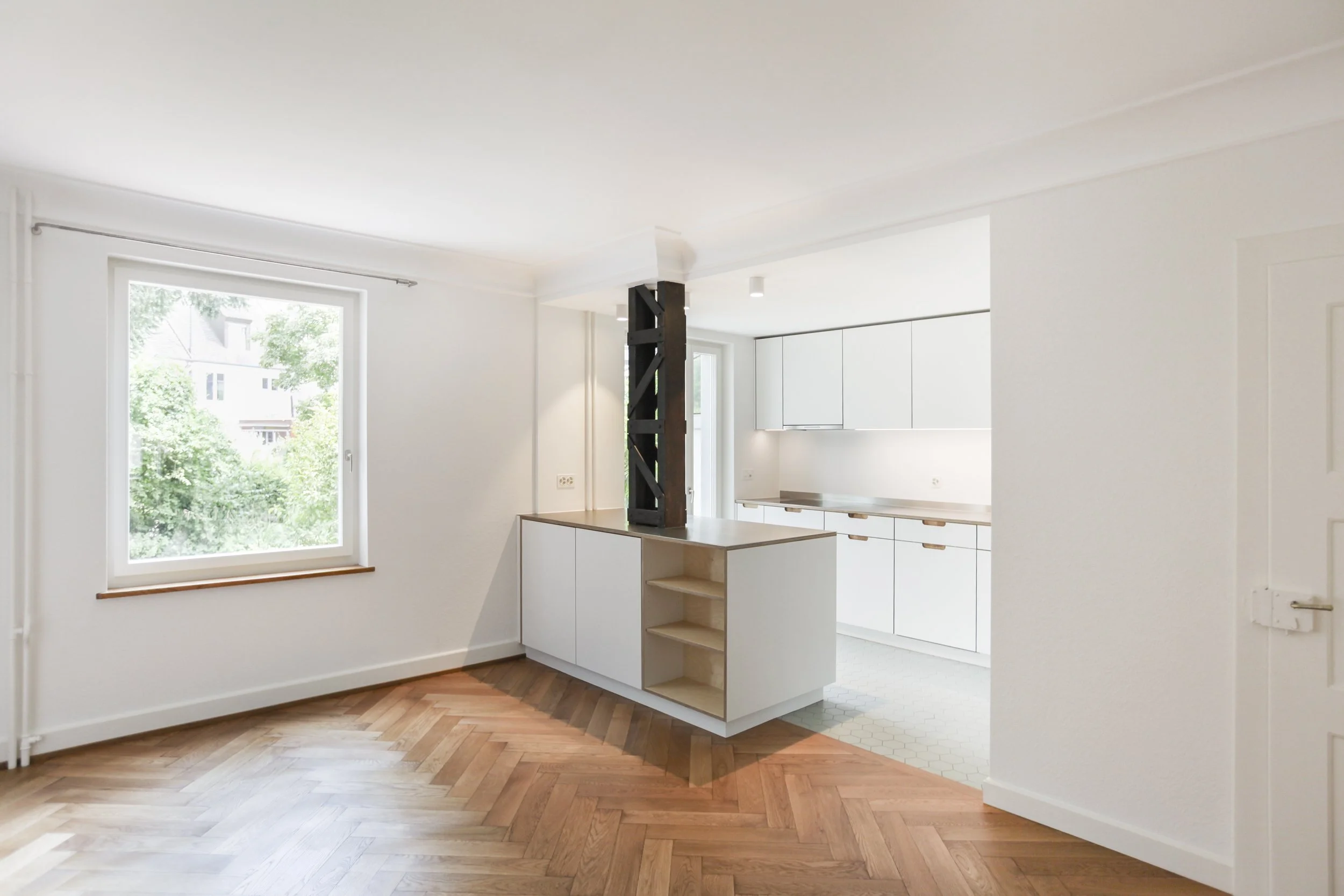 Moderner, minimalistischer Küchenraum mit weißen Schränken, Holzboden und einem großen Fenster, das viel Tageslicht reinlässt.