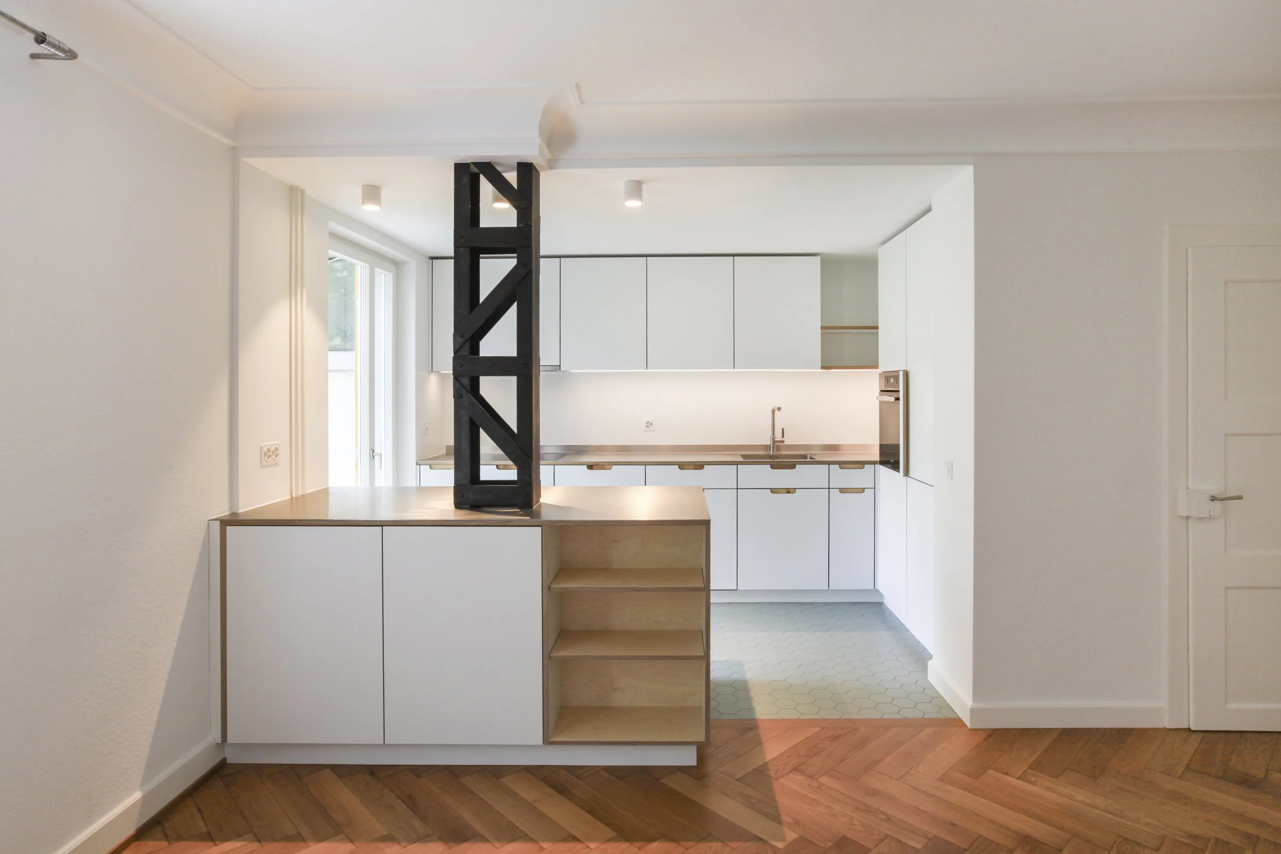 Moderne, minimalistisch ausgestattete Küchen mit weißen Schränken, Holzknöpfen, Einbaumikrowelle, Spüle mit Wasserhahn, offene Regale, Holzarbeitsplatte, dunkler strukturierter Raumteiler, helle Wände, Holzboden im Flur, weißen Tür. Natürliche Beleuc