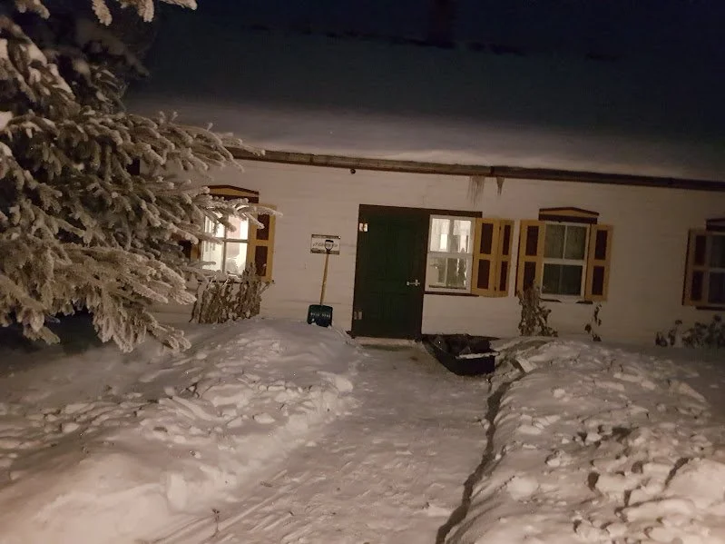Snow-covered pathway leading to the warmly lit Herdsman House at night, ideal for winter artist retreats in Manitoba.