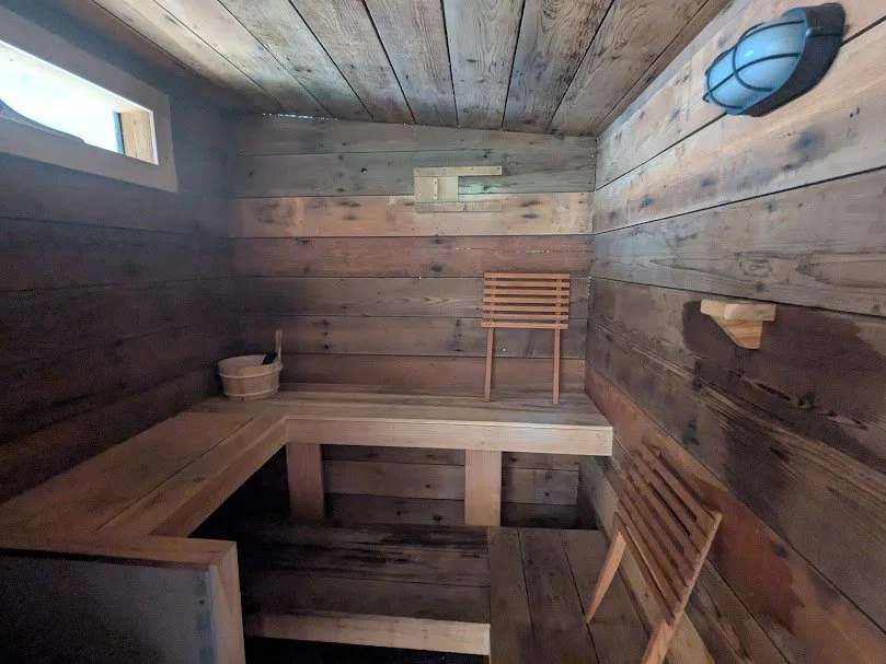 Rustic wooden sauna interior with benches, sauna stones, water bucket, and natural light—part of the Herdsman House artist retreat in Manitoba.