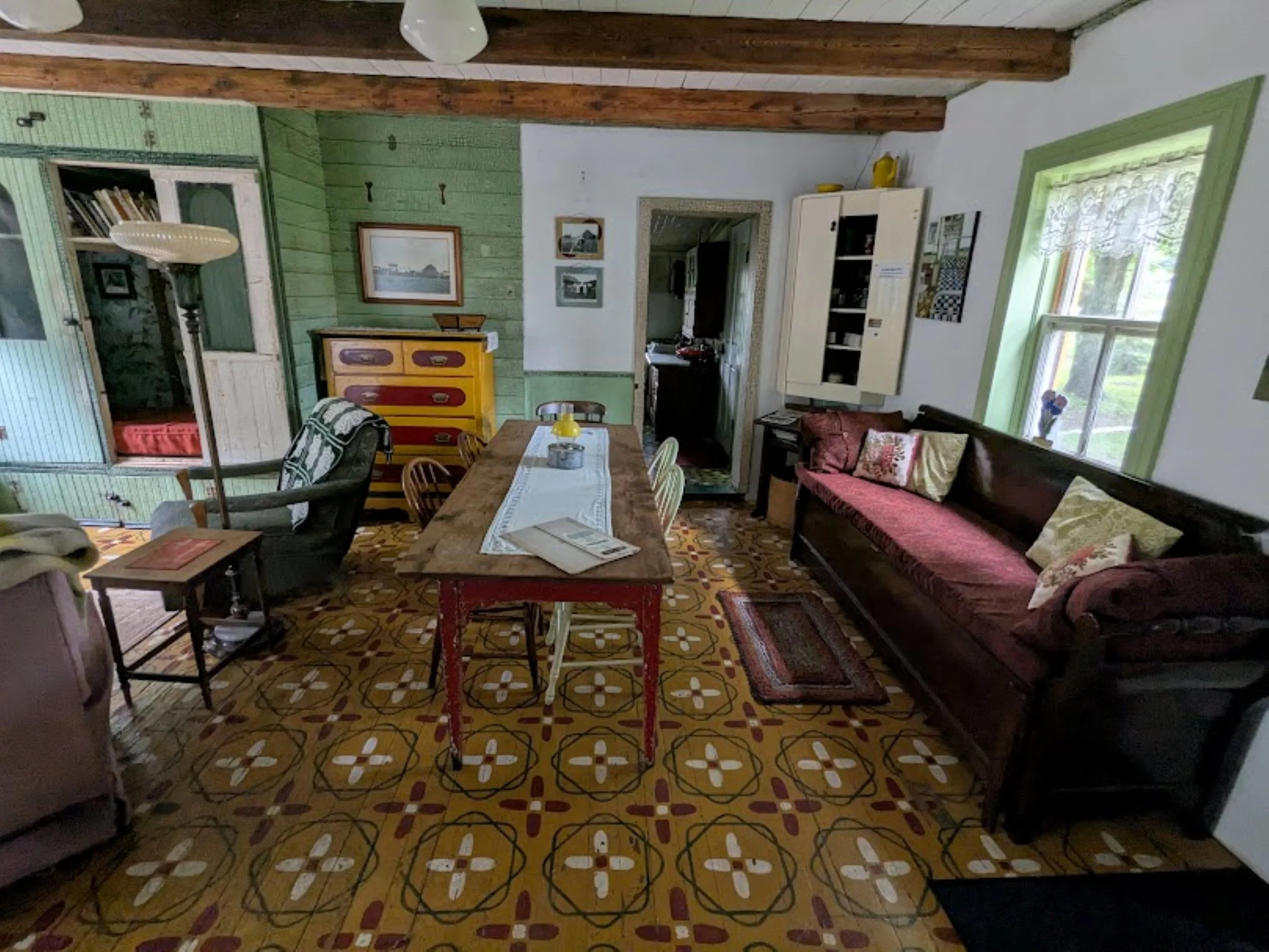 Eclectic living and dining area at Herdsman House with restored hand-painted Mennonite tile floors, mismatched vintage furniture, and rustic decor.
