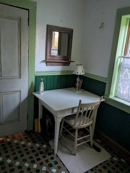 Vintage writing desk and chair in a rustic corner of Herdsman House, set against green paneled walls and restored hand-painted Mennonite floor tiles