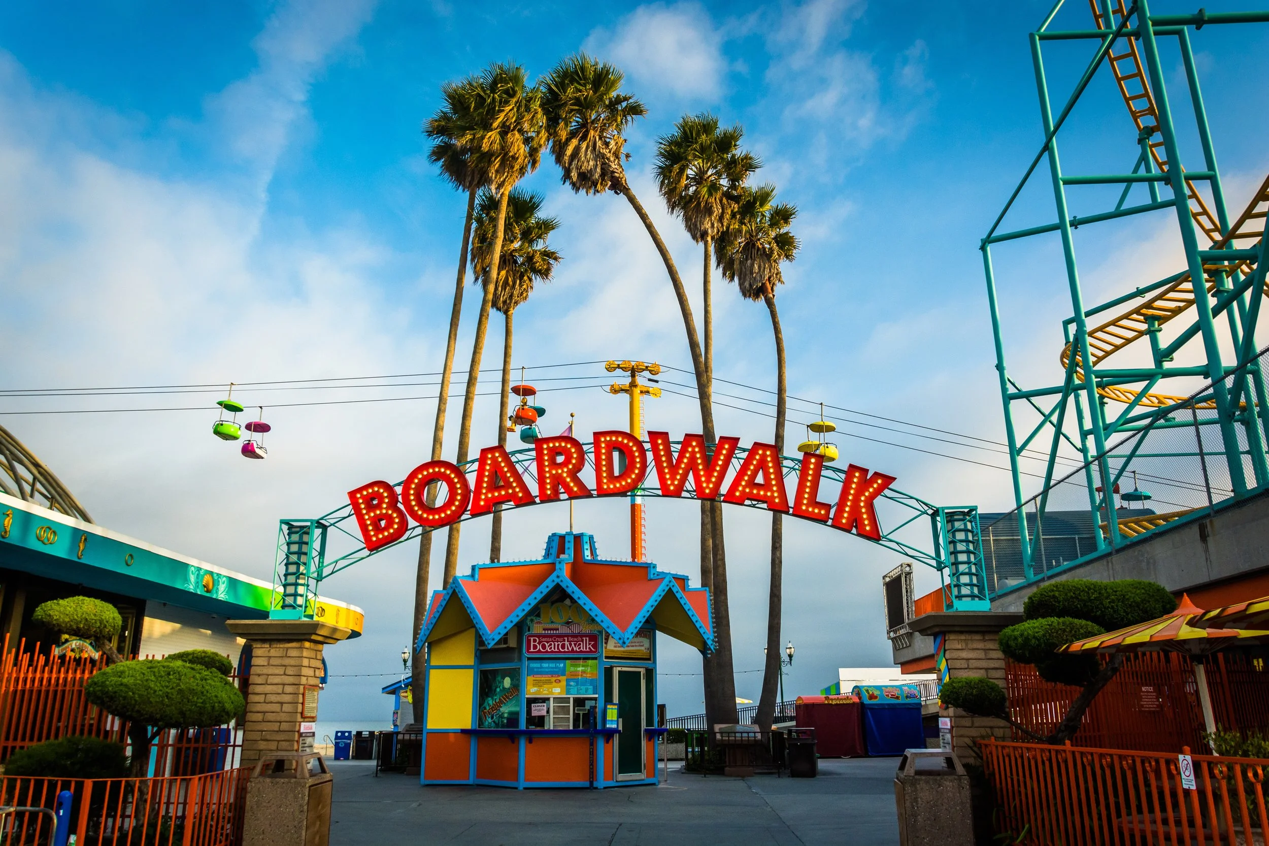 Boardwalk amusement in Santa Cruz, California  park entrance with colorful sign, palm trees, and a ridescape in the background.