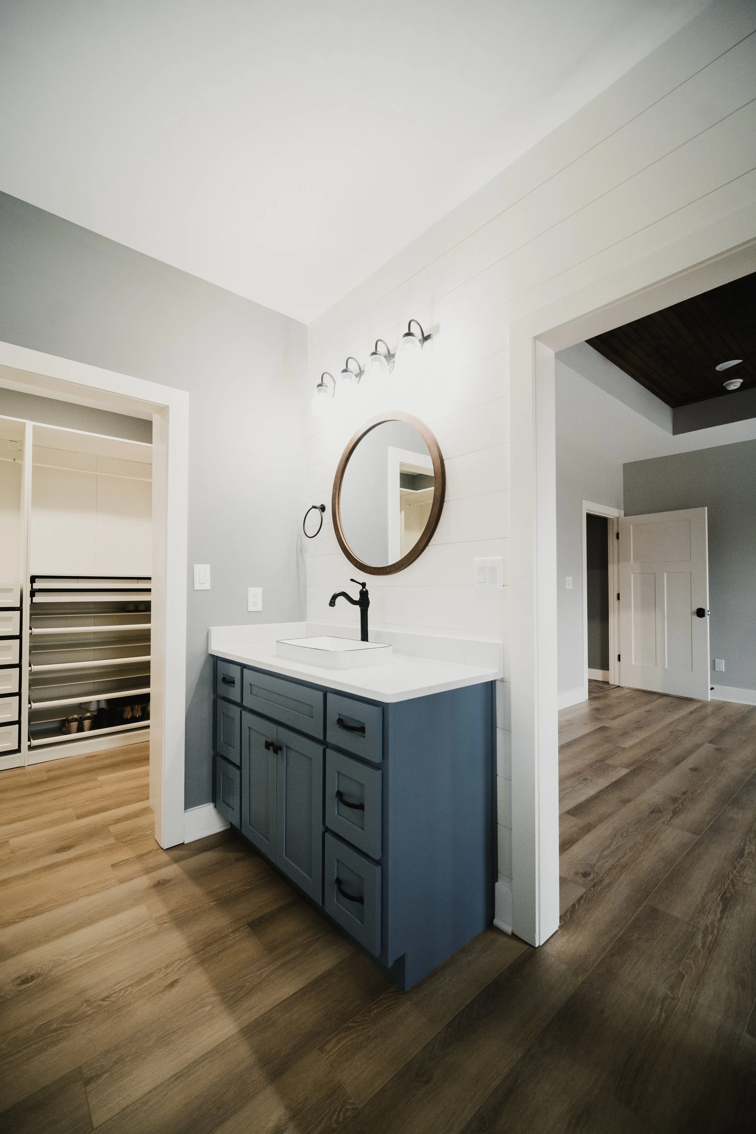 Bathroom vanity with blue cabinets, white countertop, black faucet, round mirror, and wall-mounted light fixture.