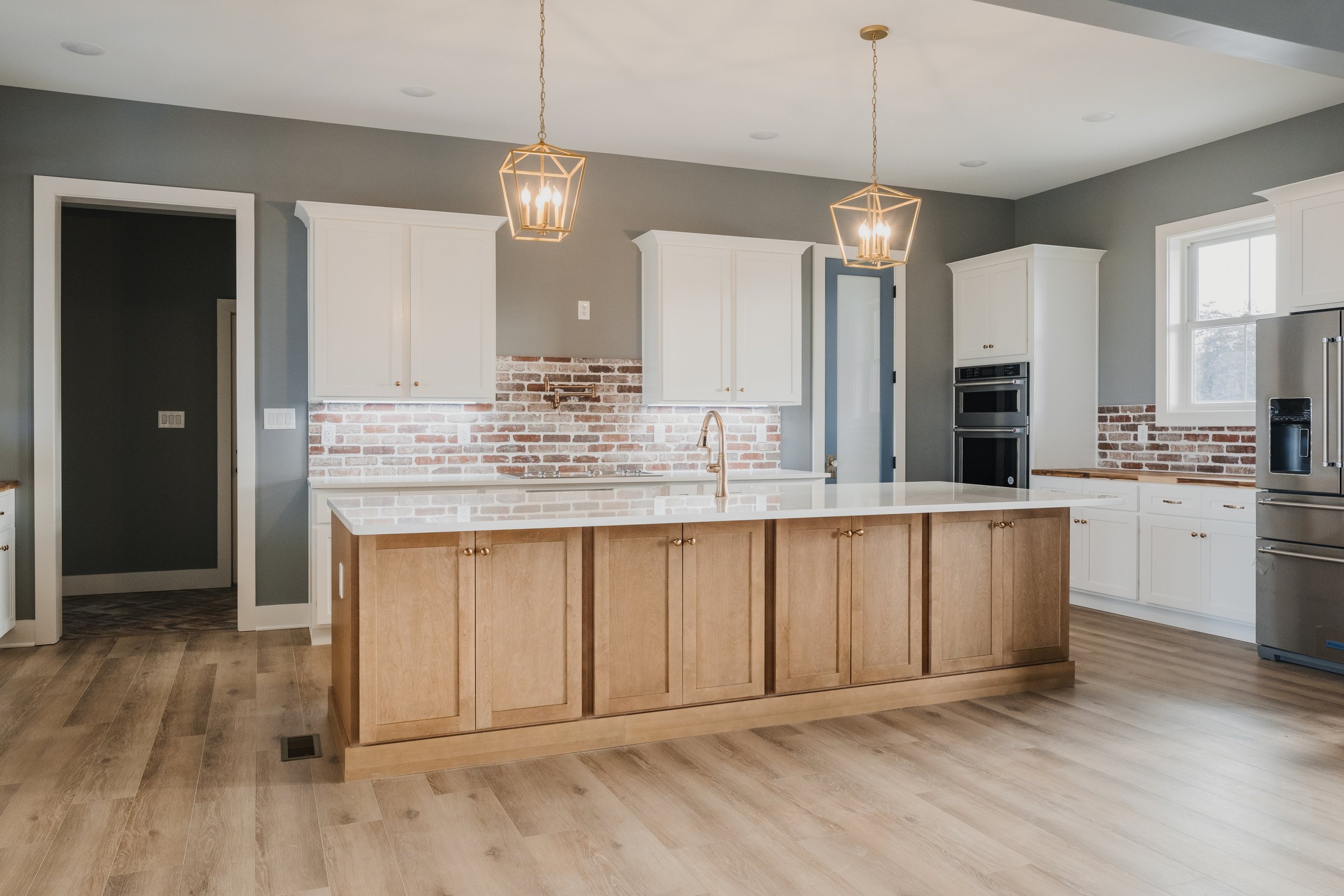 Modern kitchen with white cabinets, a large wooden island, exposed brick backsplash, pendant lighting, and stainless steel appliances.
