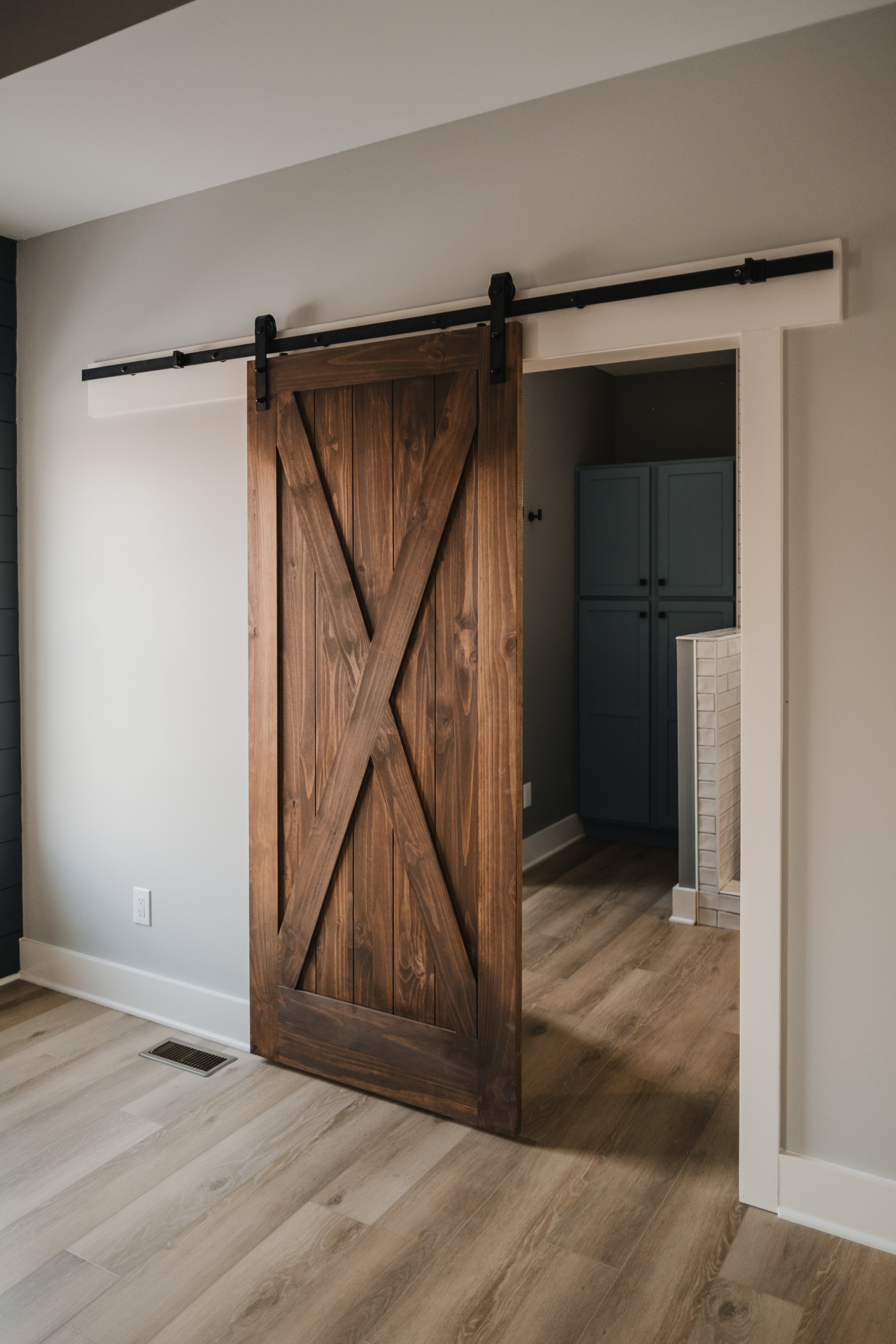 A rustic wooden sliding barn door partially open, revealing a room with blue cabinets and white brick accents.