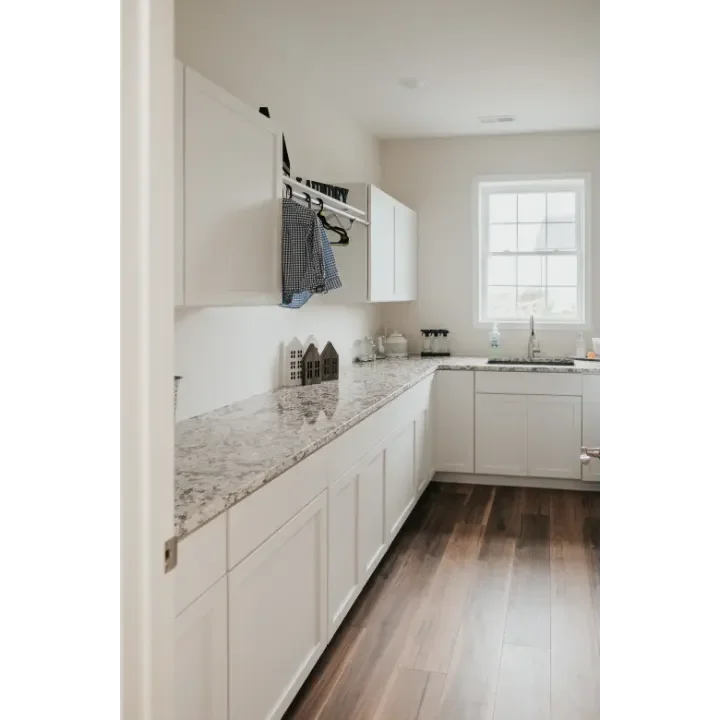 Clean, white kitchen with granite countertops, white cabinets, a window above the sink, and hardwood flooring.