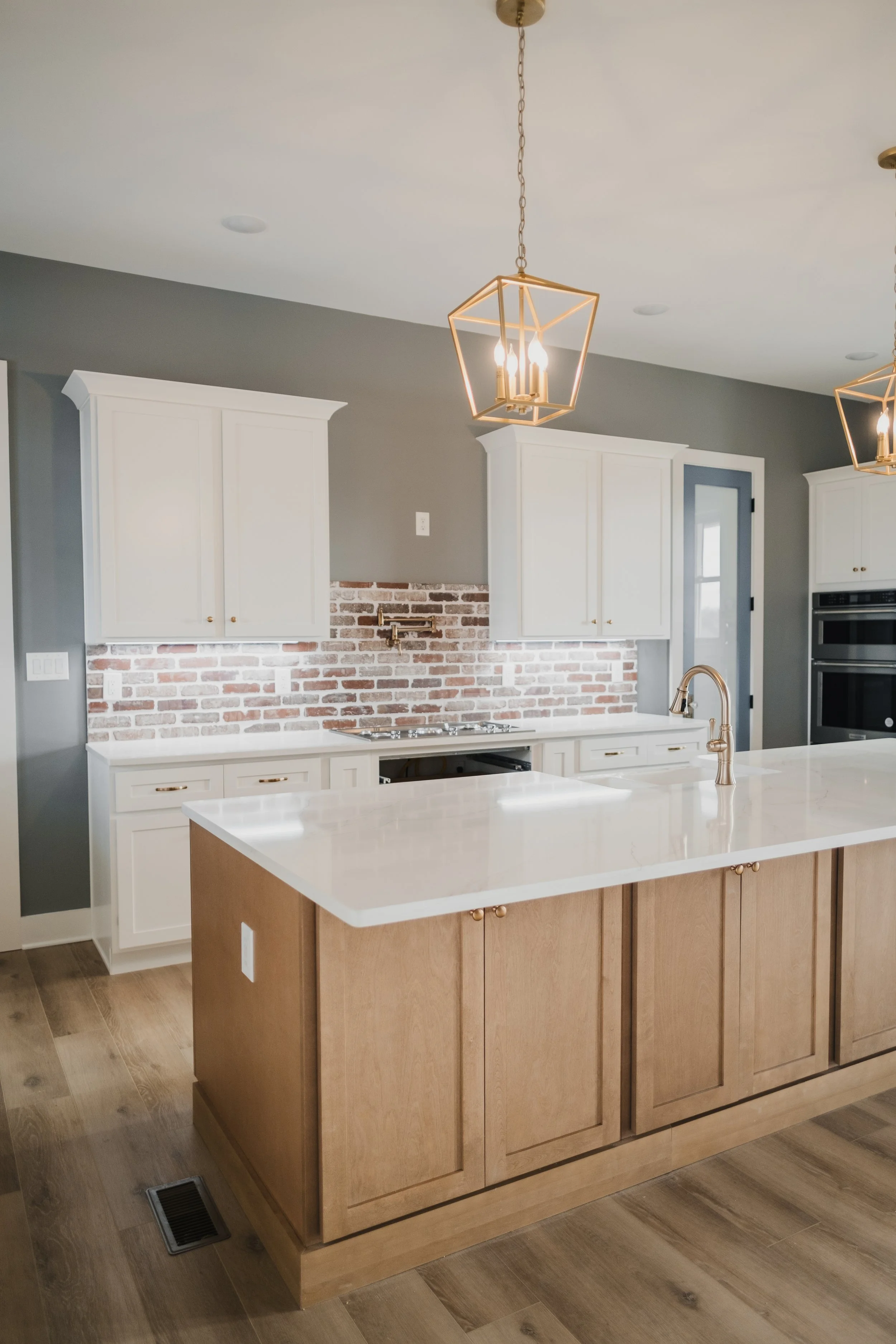 Modern kitchen with white upper cabinets, a brick backsplash, a wooden kitchen island with a white countertop, and ceiling lights.