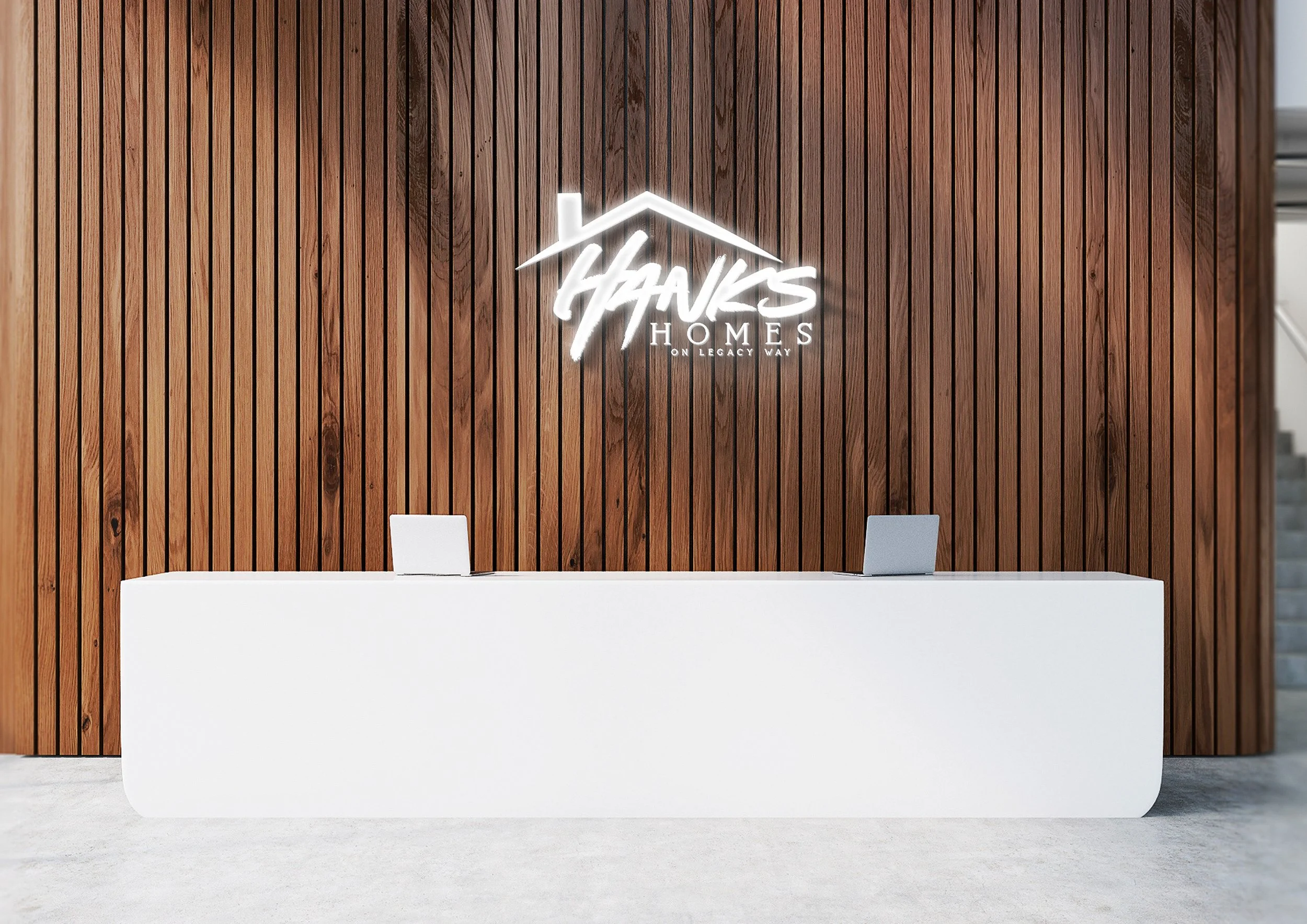 Modern reception desk in front of a wooden panel wall with a illuminated logo that reads 'Hanks Homes on Legacy Way' and a stylized house roof above the text.