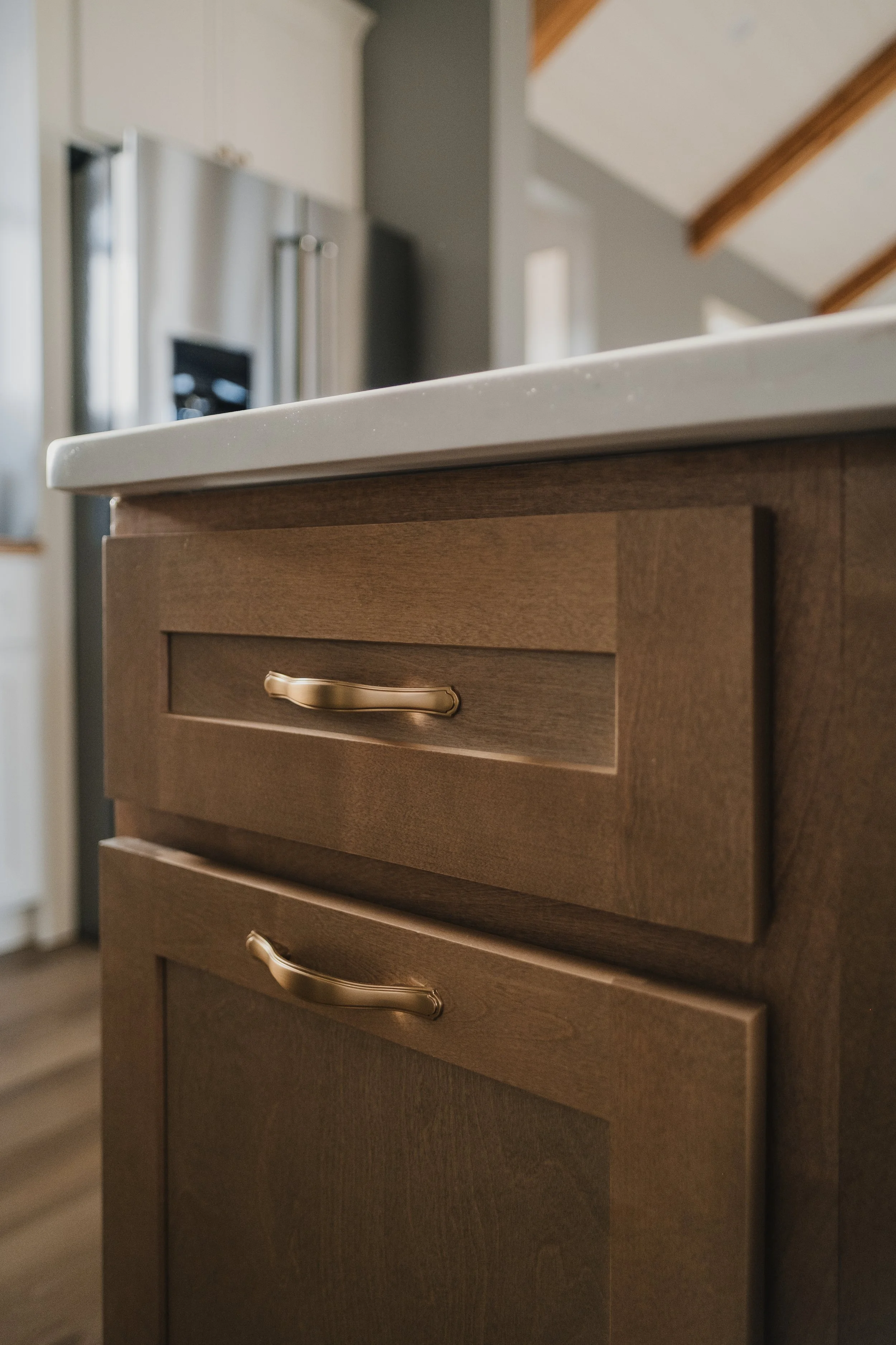 Close-up of a wooden kitchen cabinet with a white countertop and gold handles.