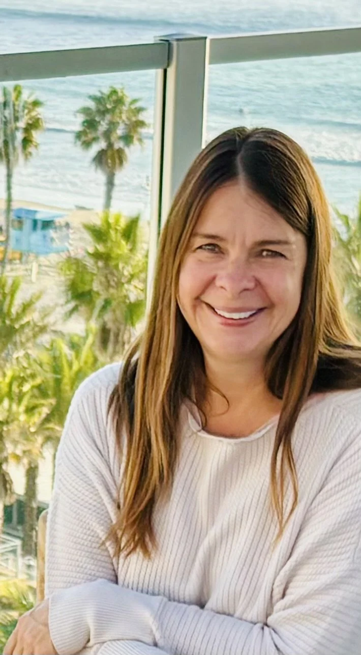 Company owner, friendly, sitting on a balcony in San Diego overlooking the ocean, with palm trees in the background.