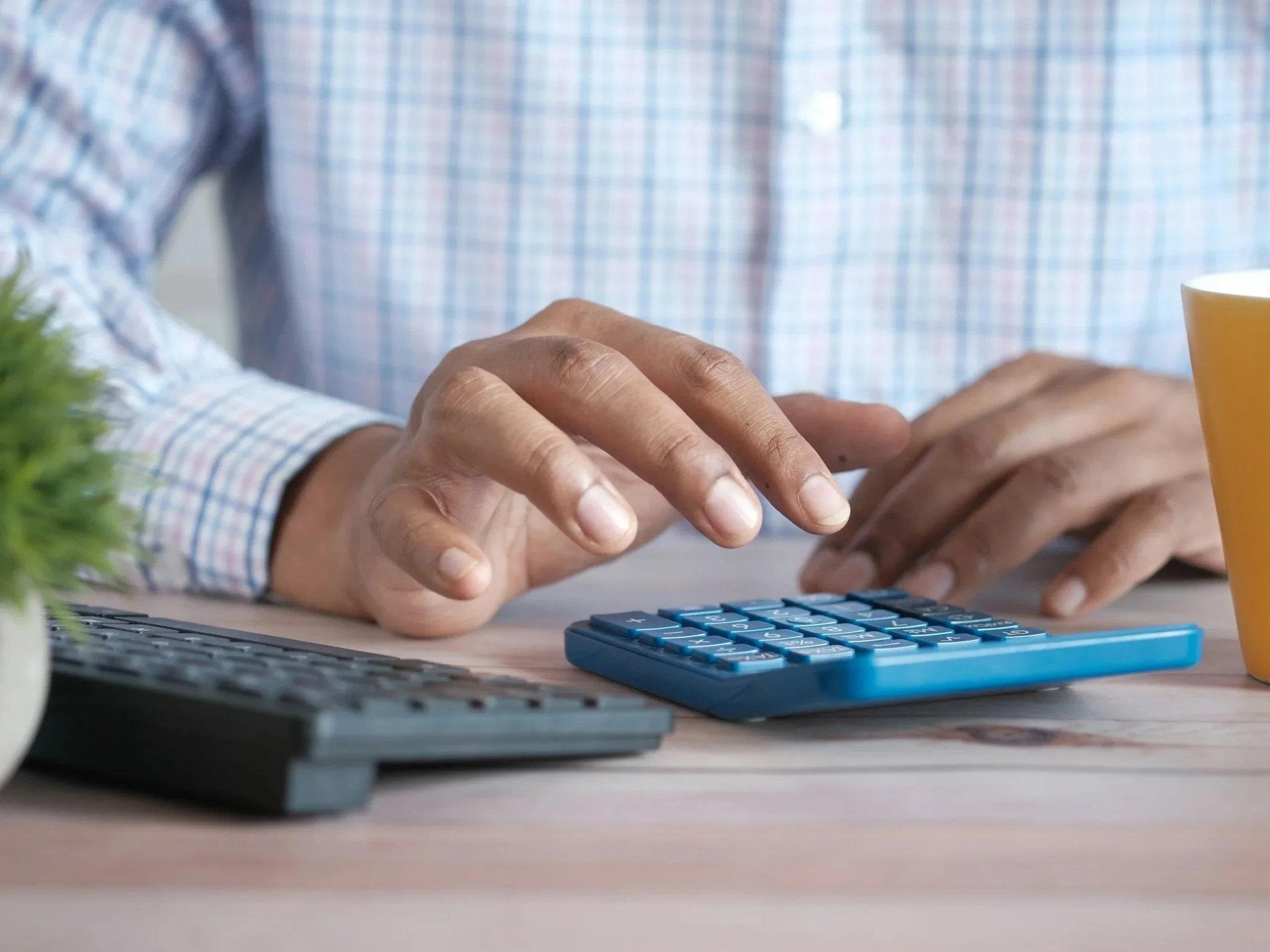 A person in a plaid shirt working at a desk with a calculator, keyboard, and a cup of orange juice.