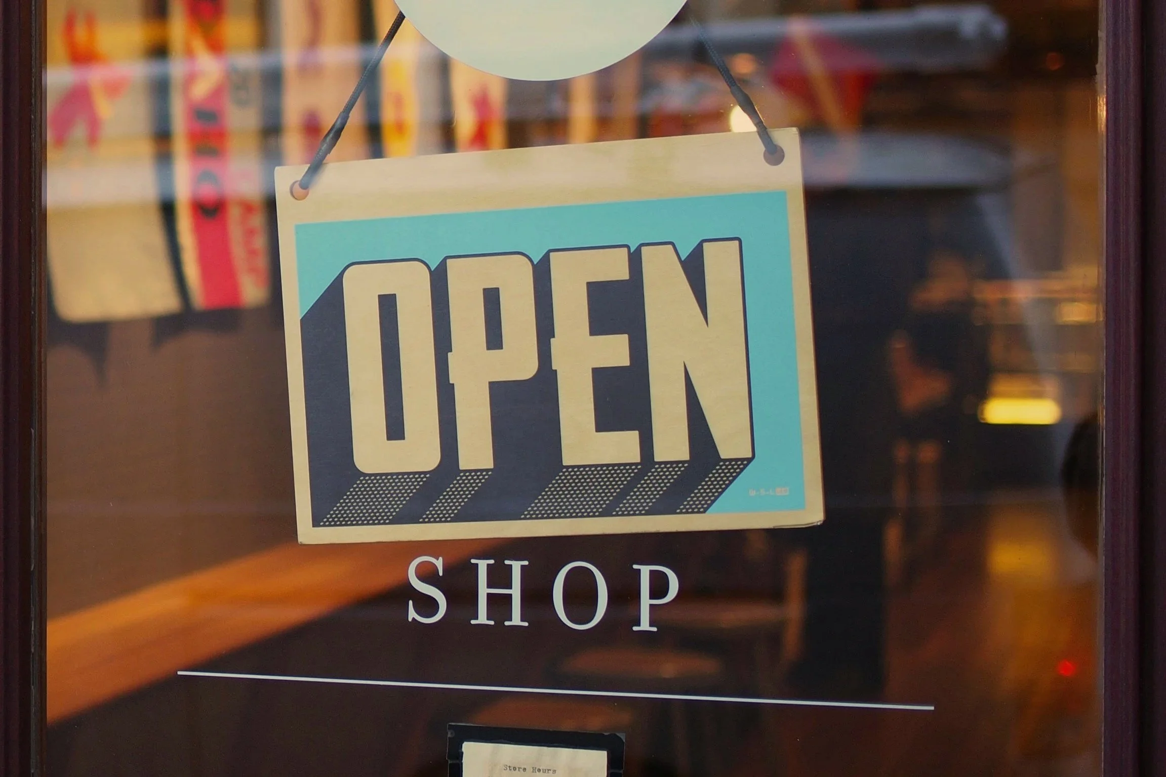 An 'Open' sign hanging in a store window with the word 'SHOP' written below.