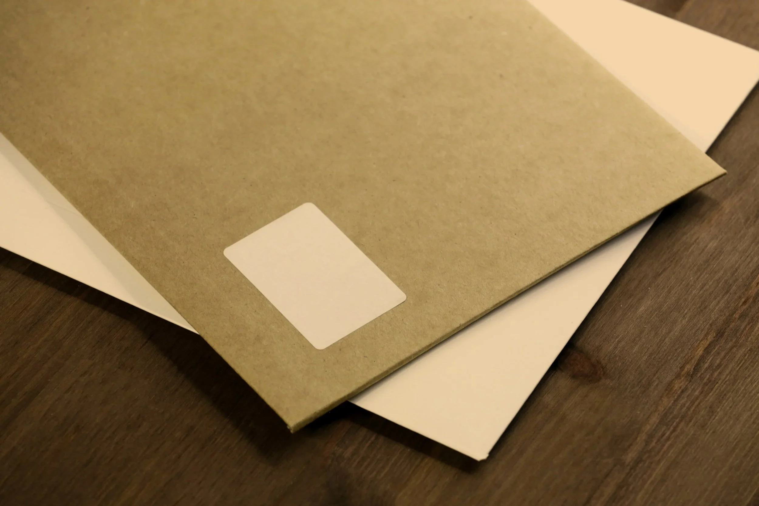 A brown folder with a blank white label on a wooden surface, partially covering a white sheet of paper.