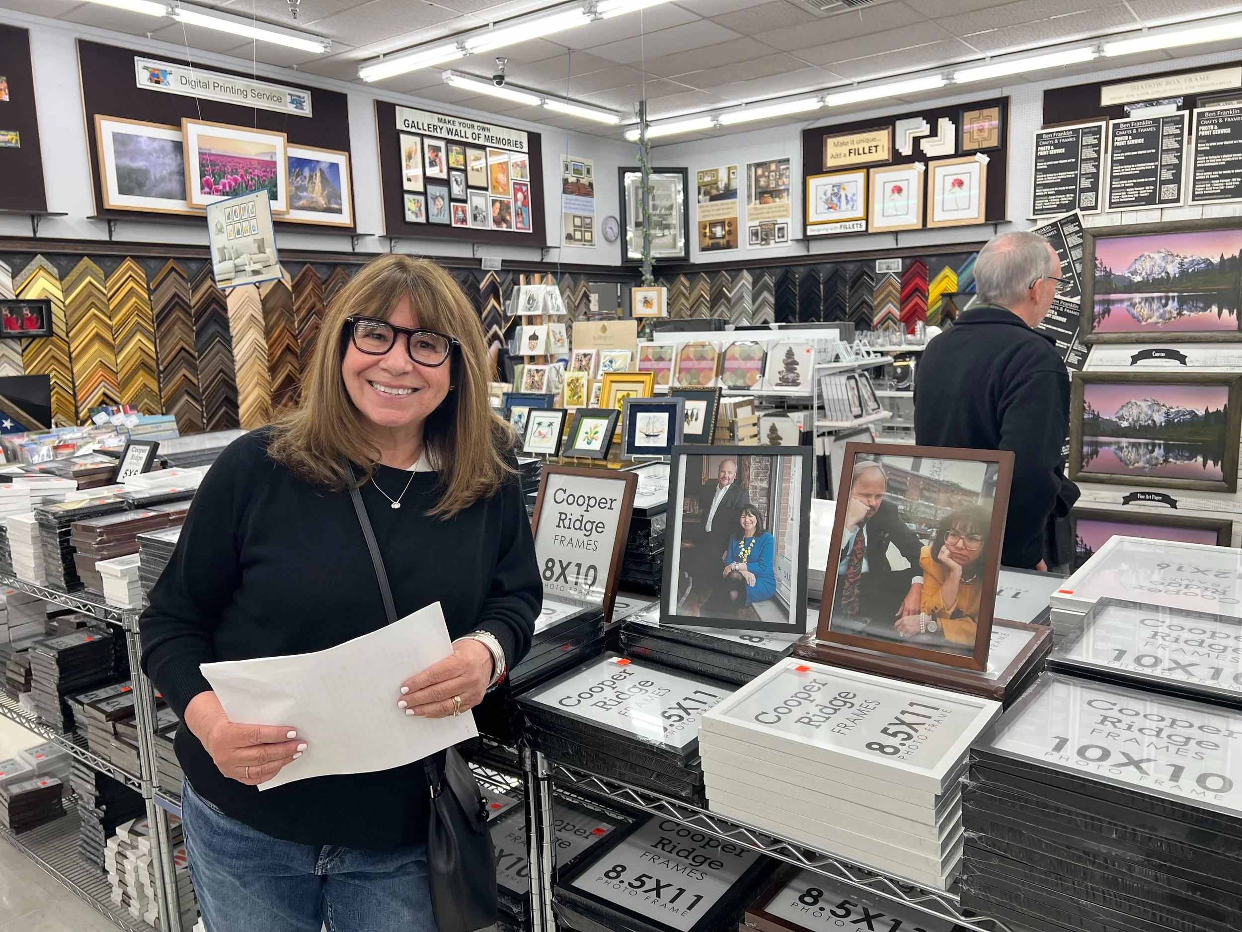 Georganne Bender doing a store tour. Behind her are framed pictures, photo frames, and wall art displayed in the store.