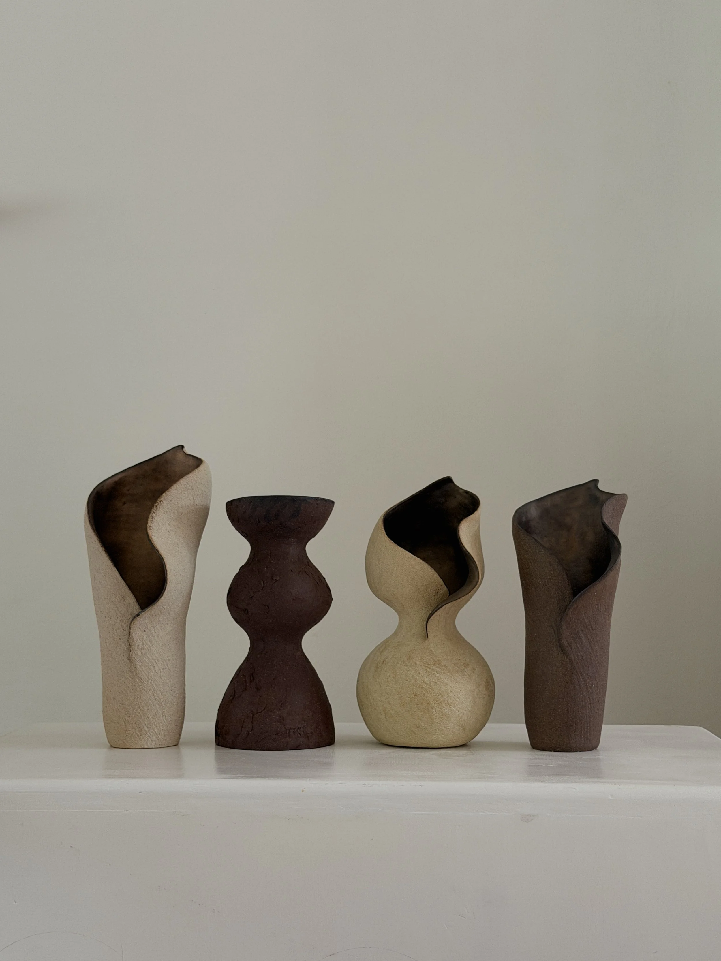 Four one-of-a-kind sculptural ceramic vases in cream and brown stoneware, in varied organic forms.