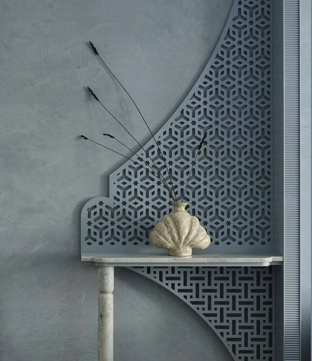 Decorative wall with geometric pattern, small white table with a shell-shaped vase holding dried flowers against a textured grey wall.