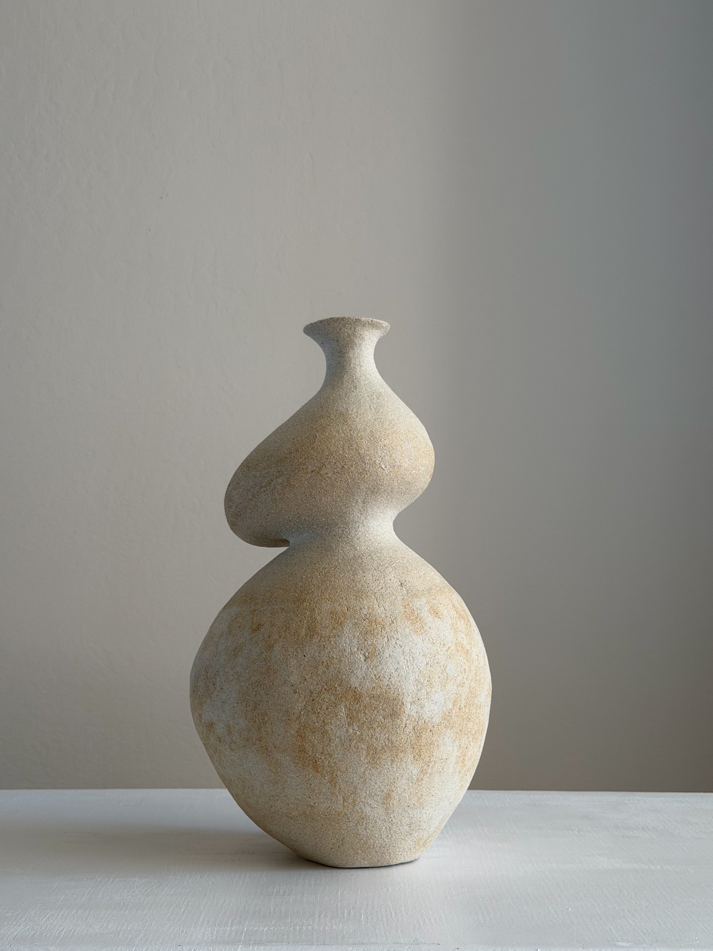 Hand-built beige stoneware vase by Anastasia Babenko with a rounded base and curved sculptural neck, in soft warm tones