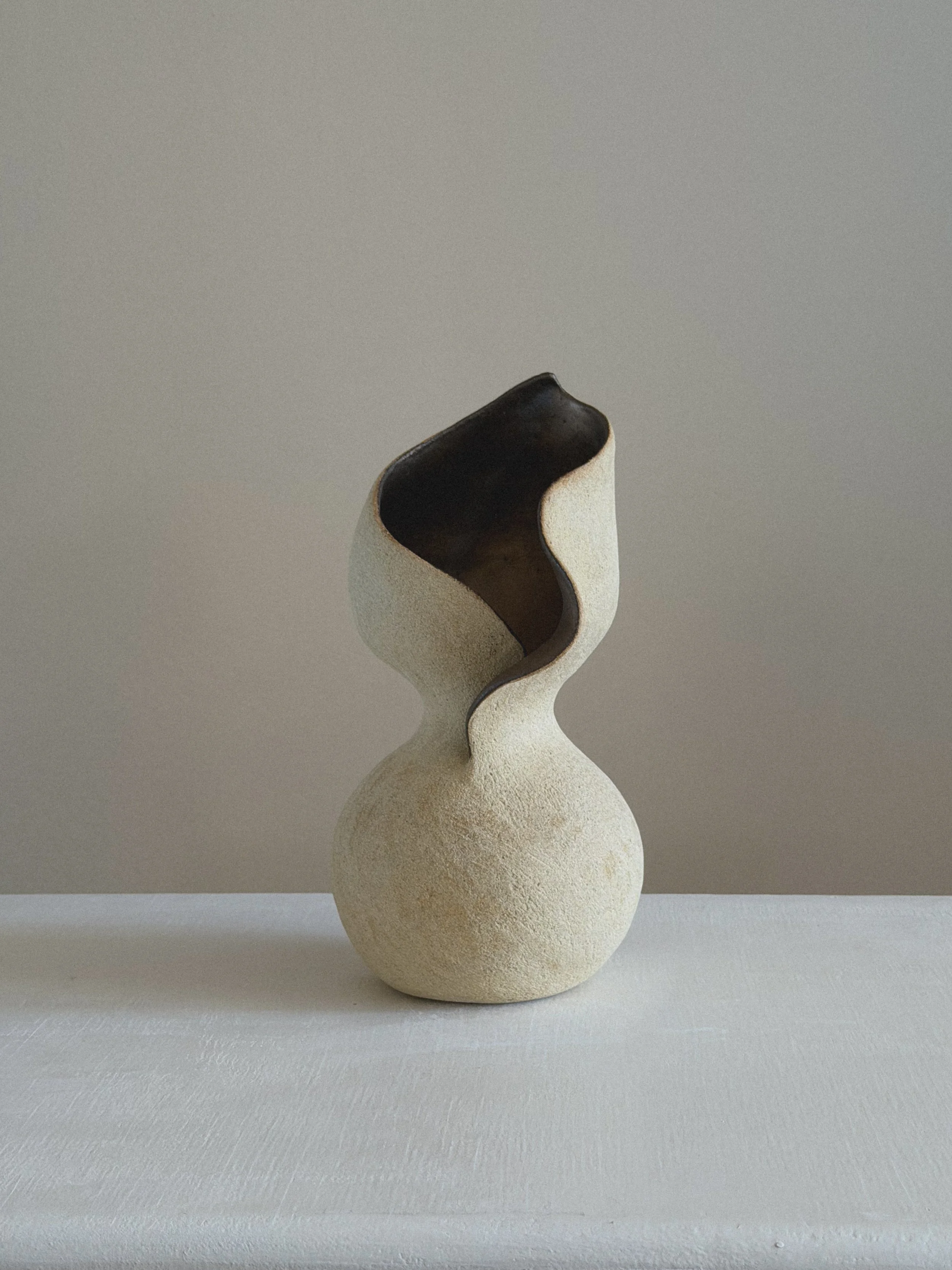 She — hand-built sculptural ceramic vessel by Anastasia Babenko with an hourglass female form, textured cream surface, and dark glazed wave-cut interior