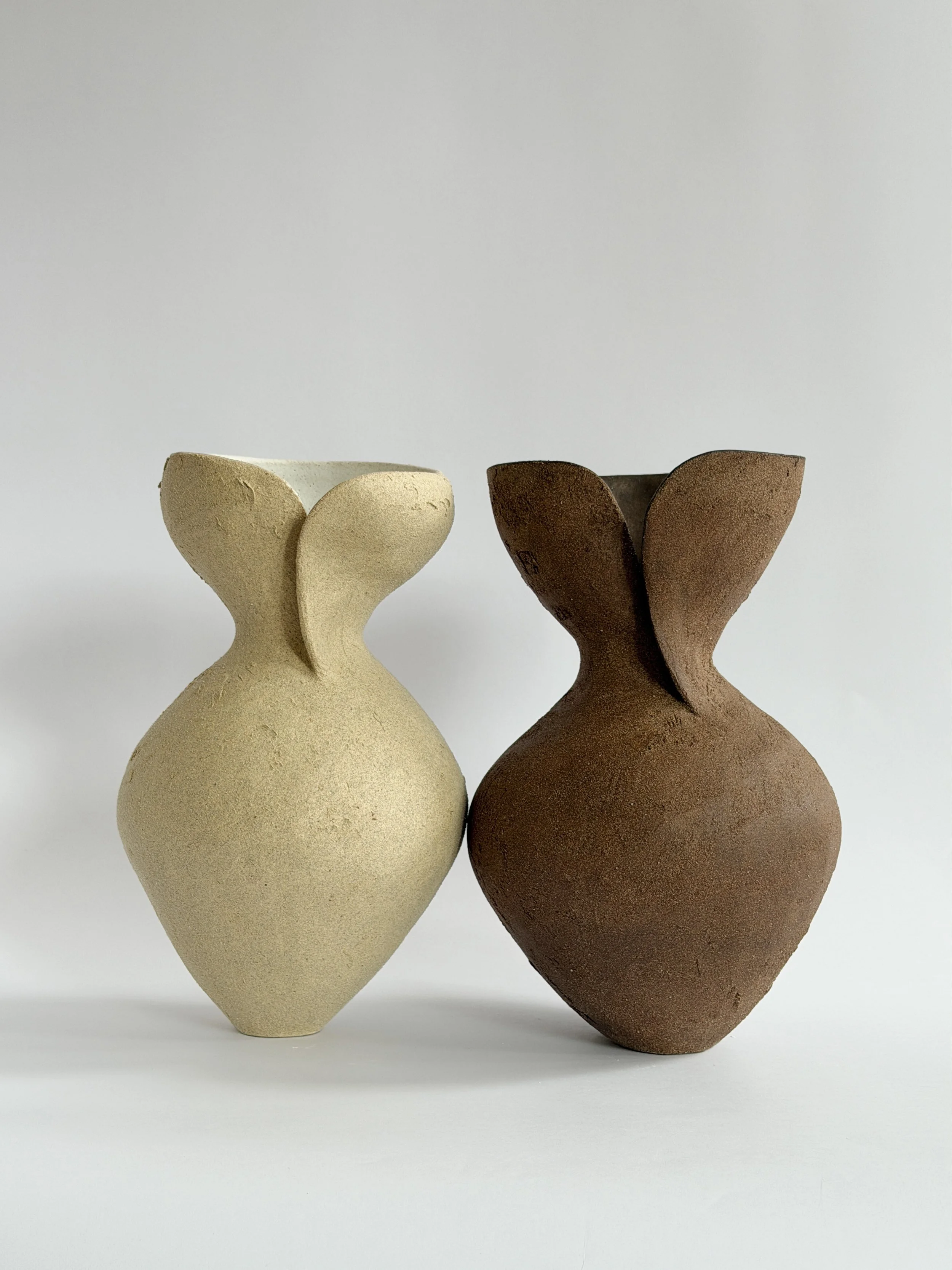 Two hand-built stoneware vases, one cream and one brown, with folded petal-like openings and rounded bodies.