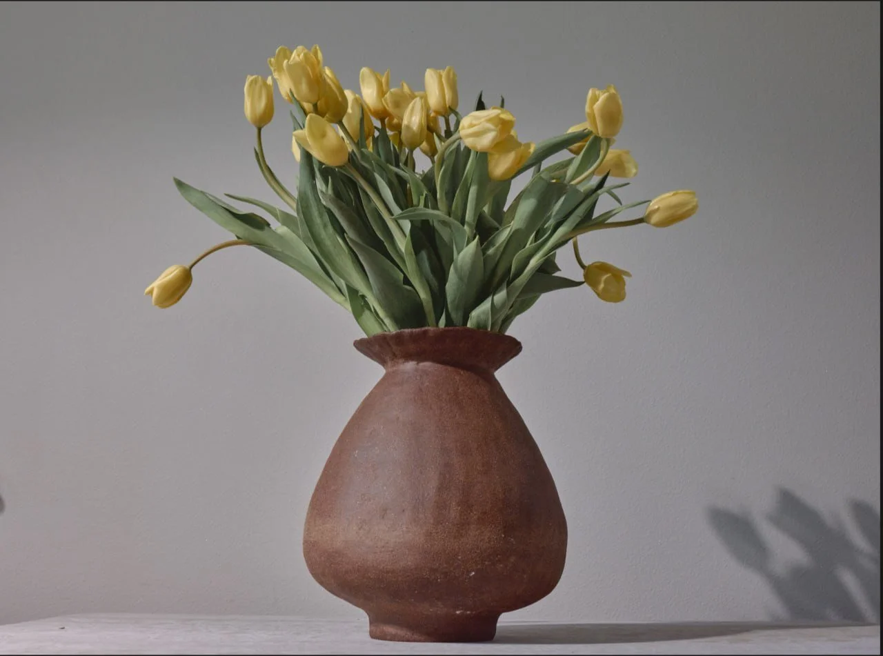 Hand-built brown stoneware vase with a ruffled rim by Anastasia Babenko, holding a bouquet of yellow tulips