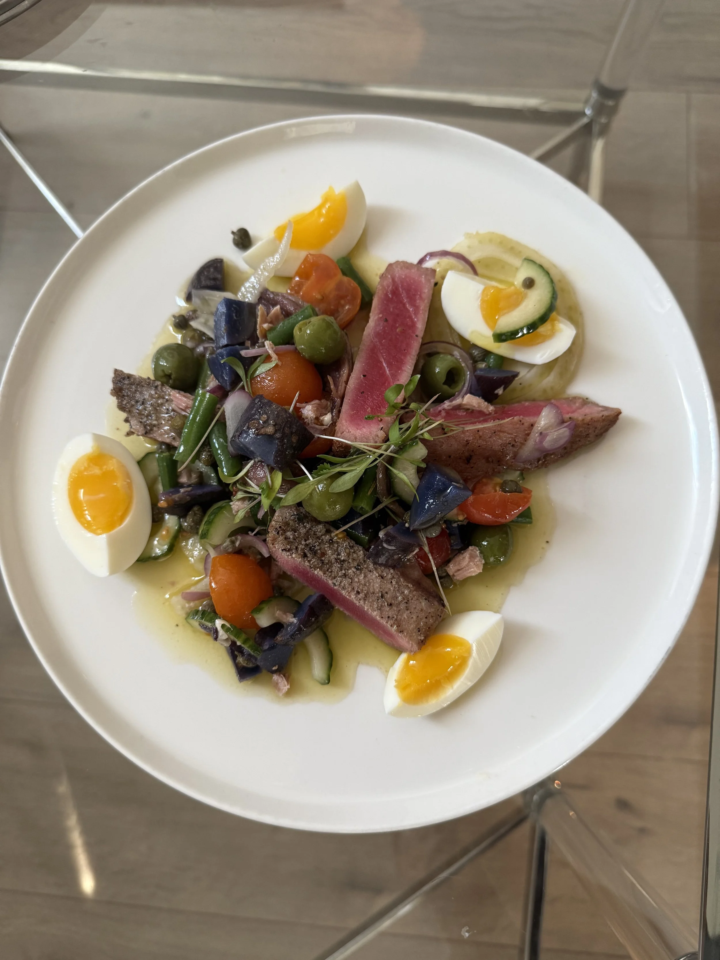 A plate of salad with sliced hard-boiled eggs, slices of steak, tomatoes, green peas, olives, and various chopped vegetables.