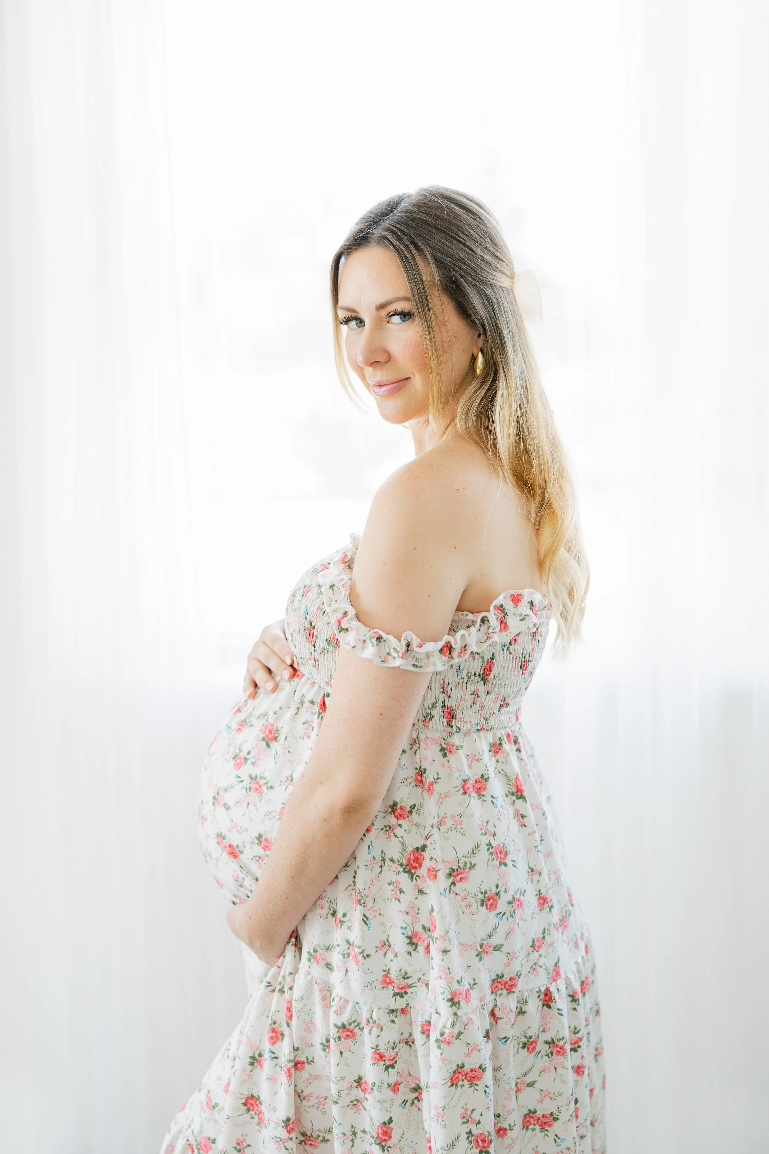 Mother to be smiling while holding baby bump in Houston maternity portrait