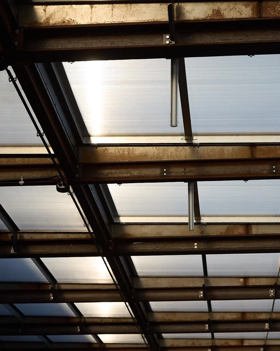 Nestled under open skies, this immense metal structure stands as a testament to time and nature's touch. Built to withstand the elements, it doesn&rsquo;t just weather the seasons; it evolves with them. The rusted steel beams and transparent roof pan