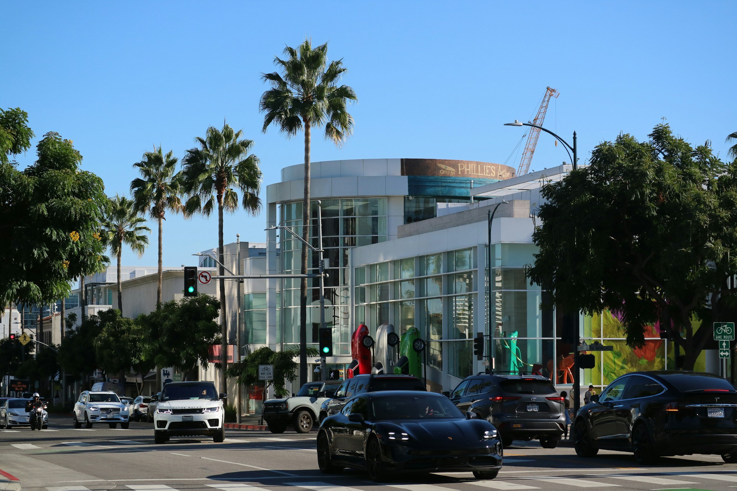 City street with cars, traffic lights, trees, and a modern building with glass windows