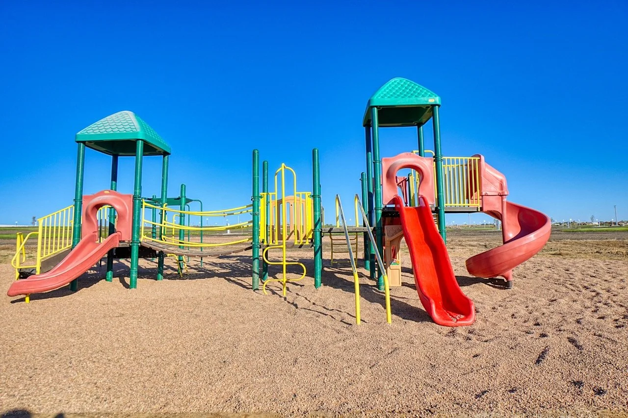 Colorful playground climbing frame and slide under sunny sky, trees in background
