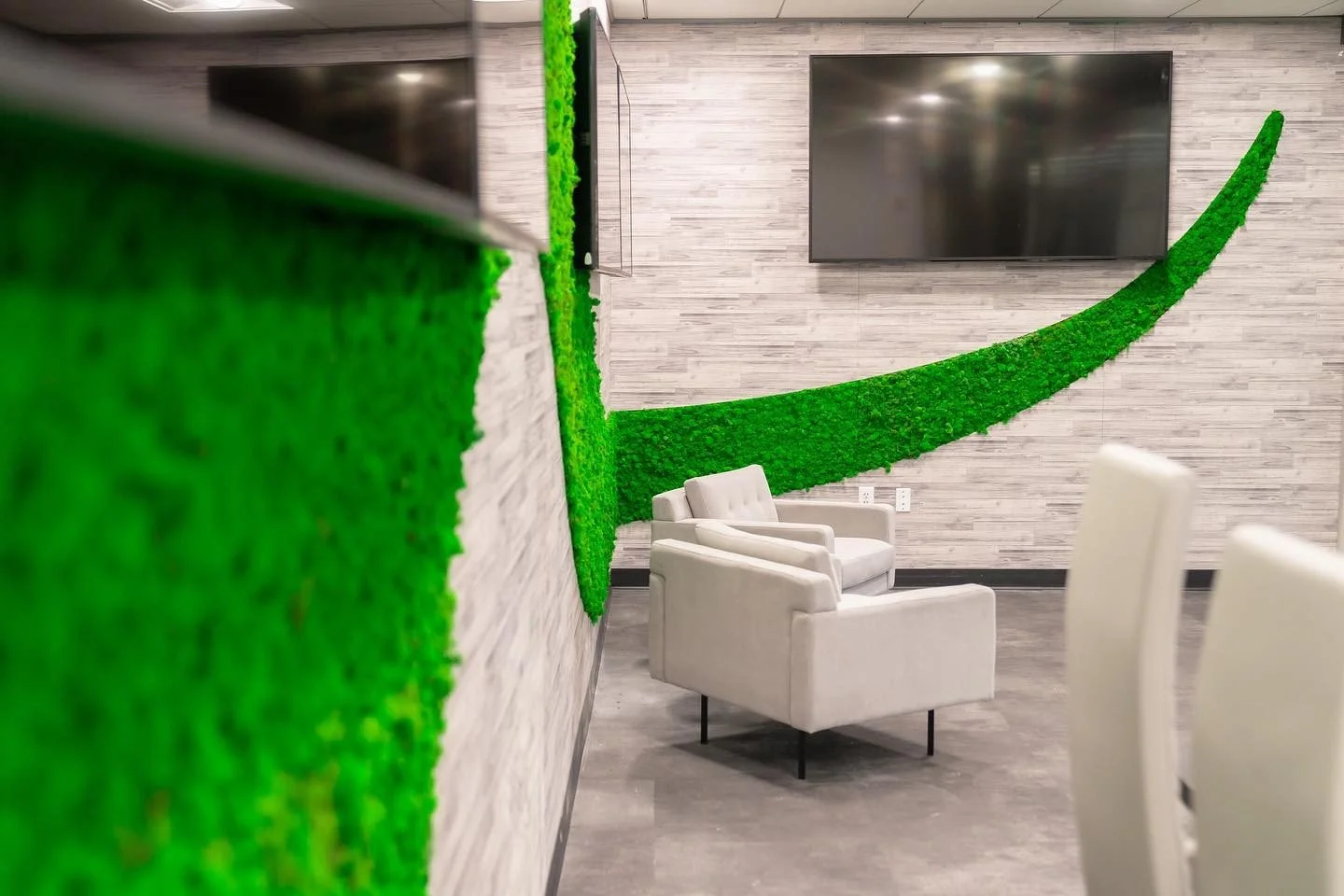 Interior of a modern lounge with a green wall decoration, white chairs, and a large TV on the wall.