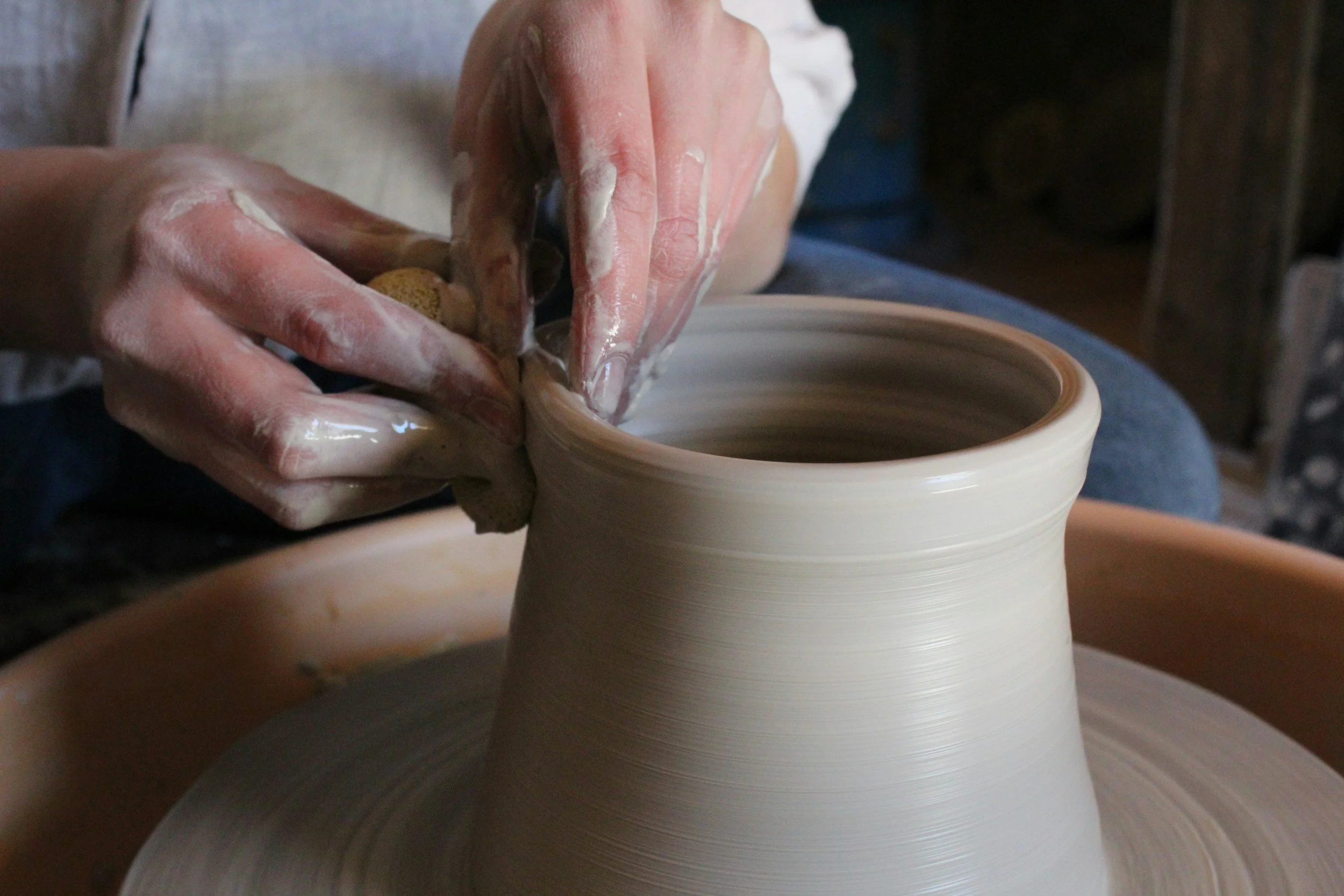 Hands shaping a clay pot on a pottery wheel in a pottery studio.