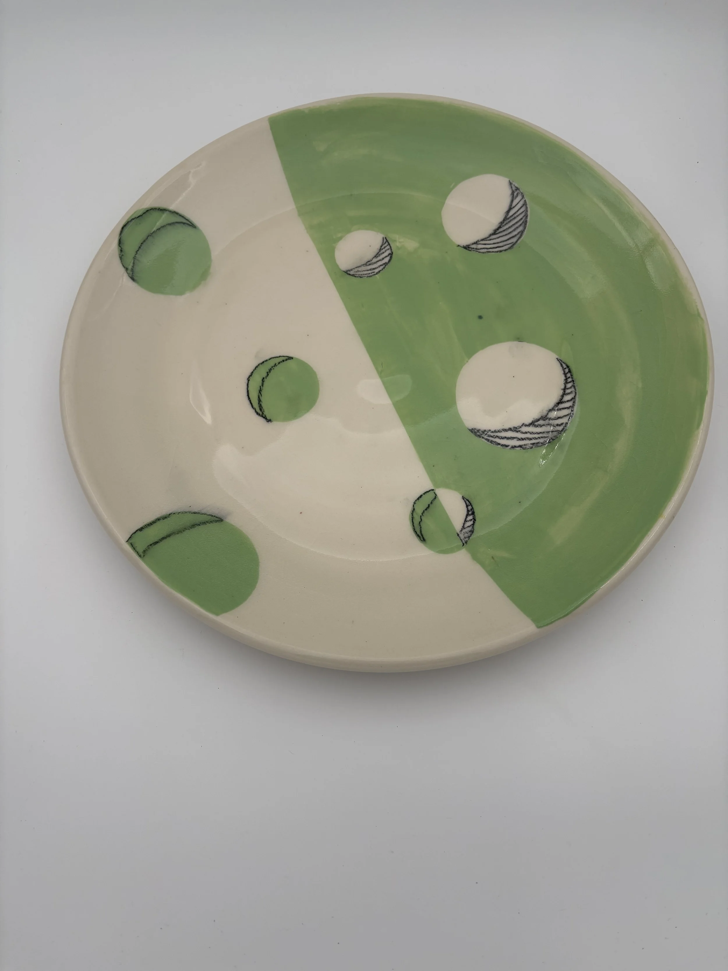 Decorative ceramic plate with abstract design of green and black circles on a cream and green background.