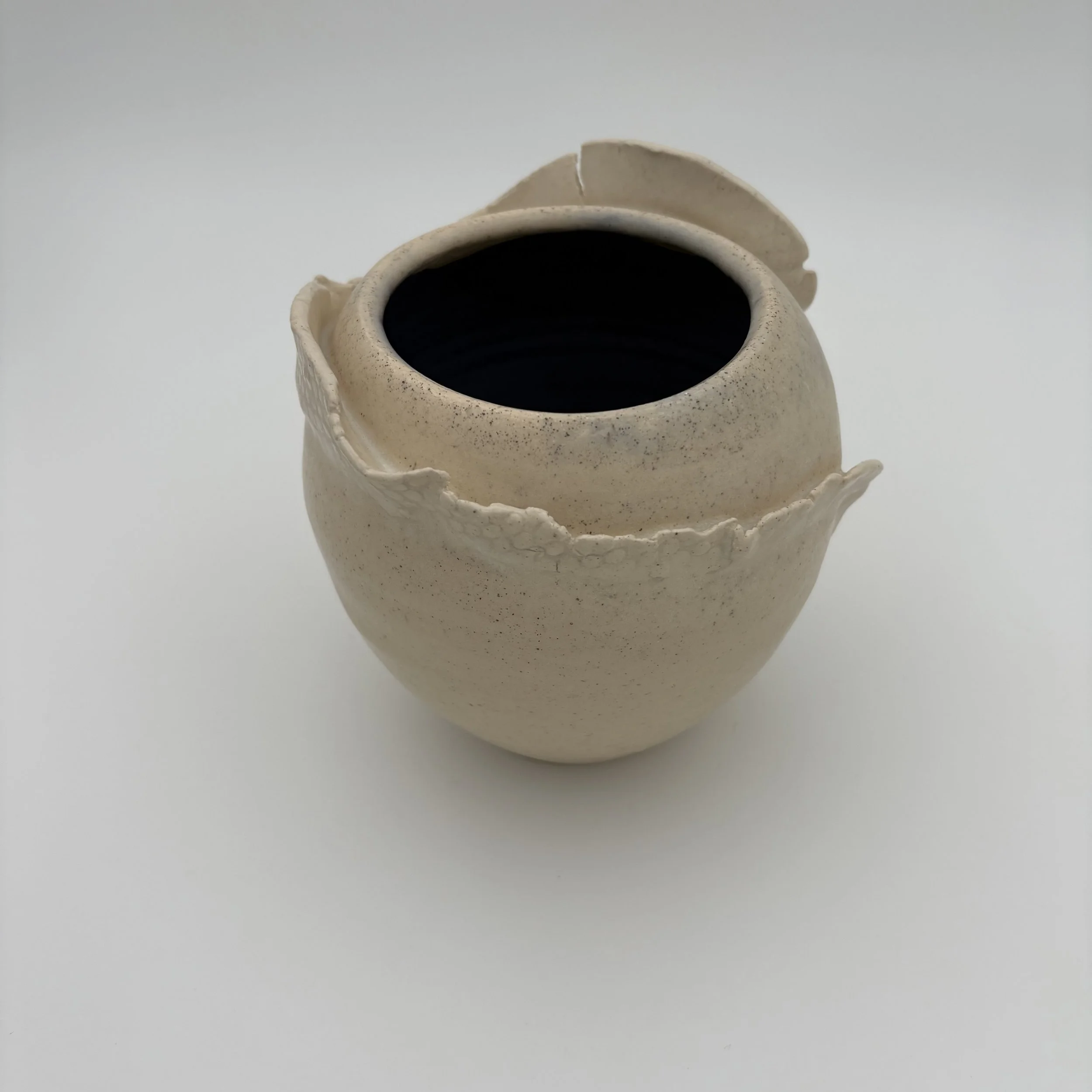 A ceramic vase with a textured, irregular edge, filled with a dark liquid, placed on a plain white background.