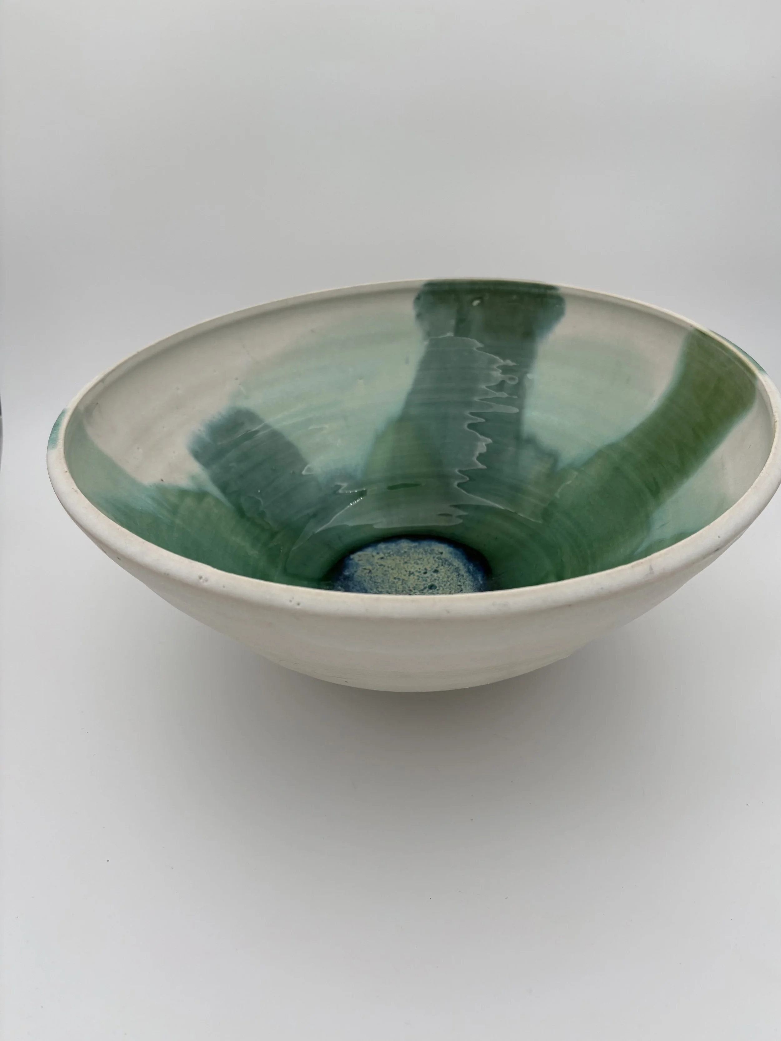 A ceramic bowl with a white exterior and green glaze interior, rested on a plain white surface.