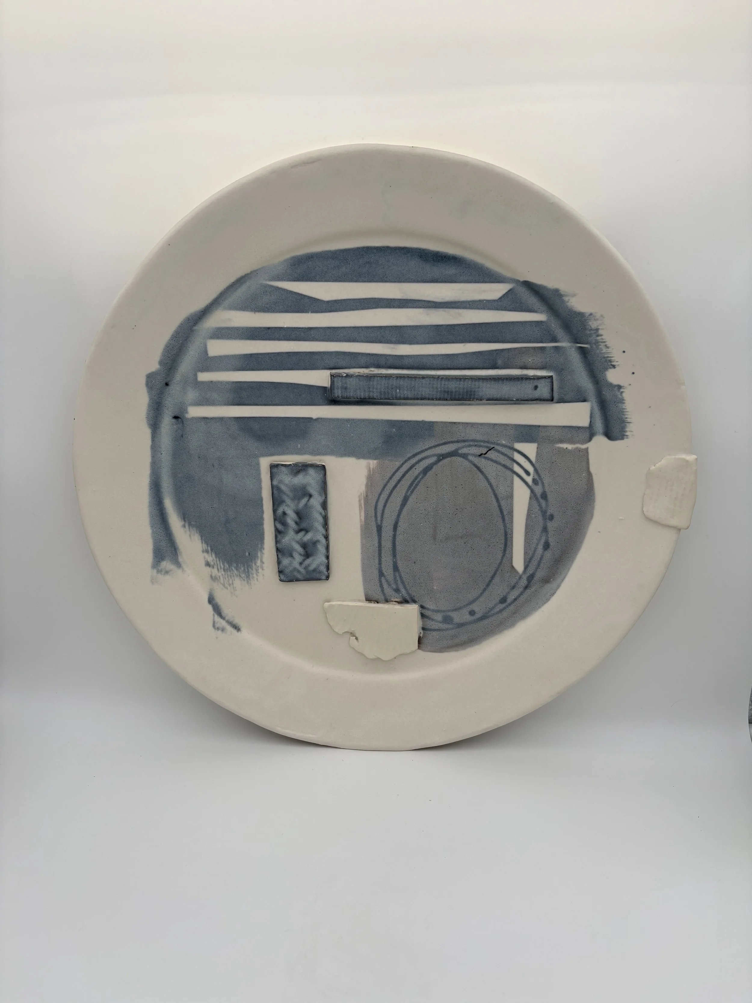Ceramic plate with abstract blue and white patterns, some broken pieces attached, on a white background.